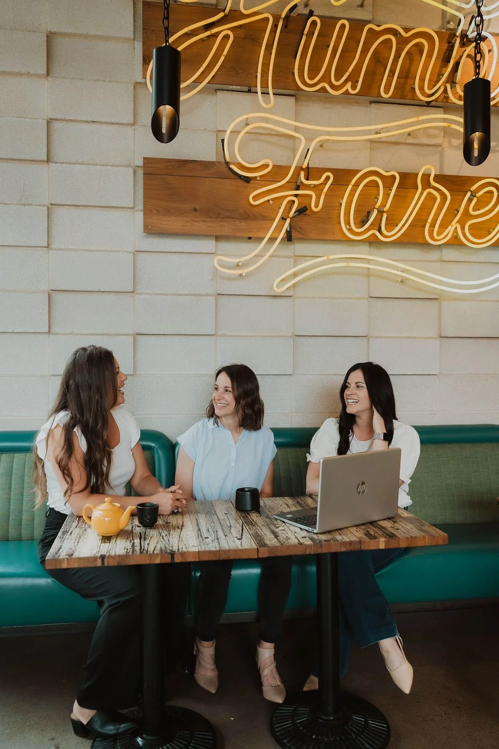The Collective for designers talks with an interior designer about building a thriving business. Three women with dark hair sit in a cafe chatting.