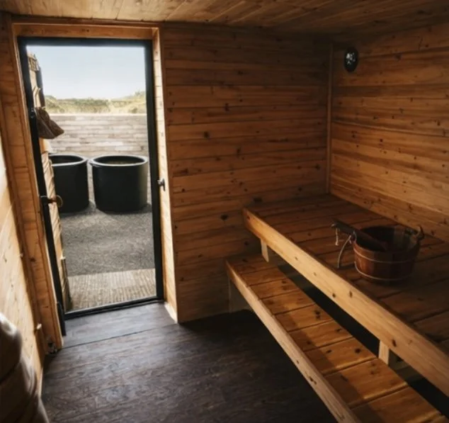 Wood-paneled sauna room with a bench, a bucket, and an outside view of the yard with two large black containers
