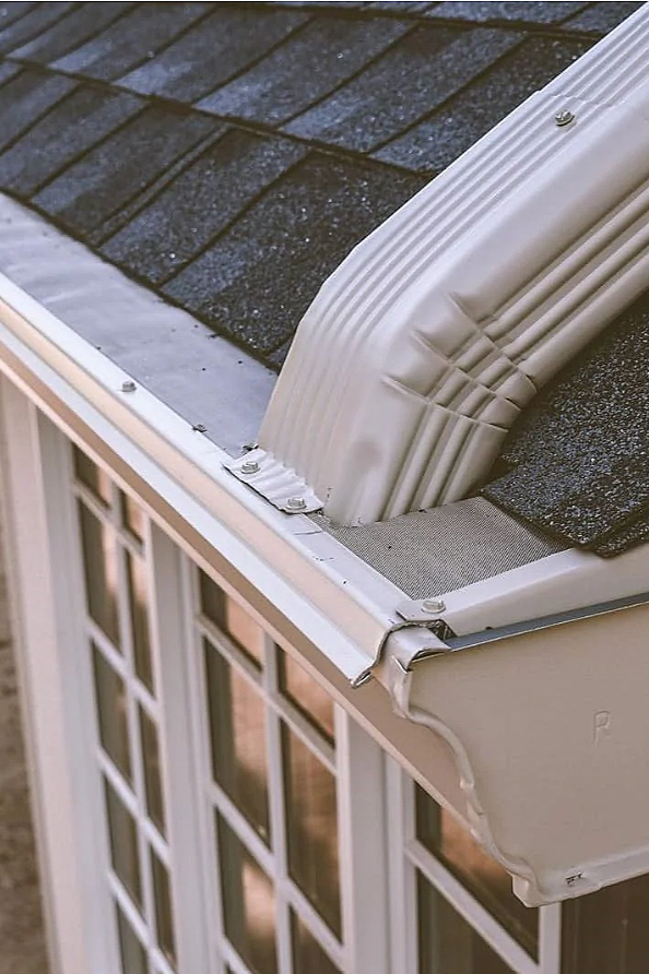 Close-up of a house roof gutter system, showing the gutter, downspout, and shingles.