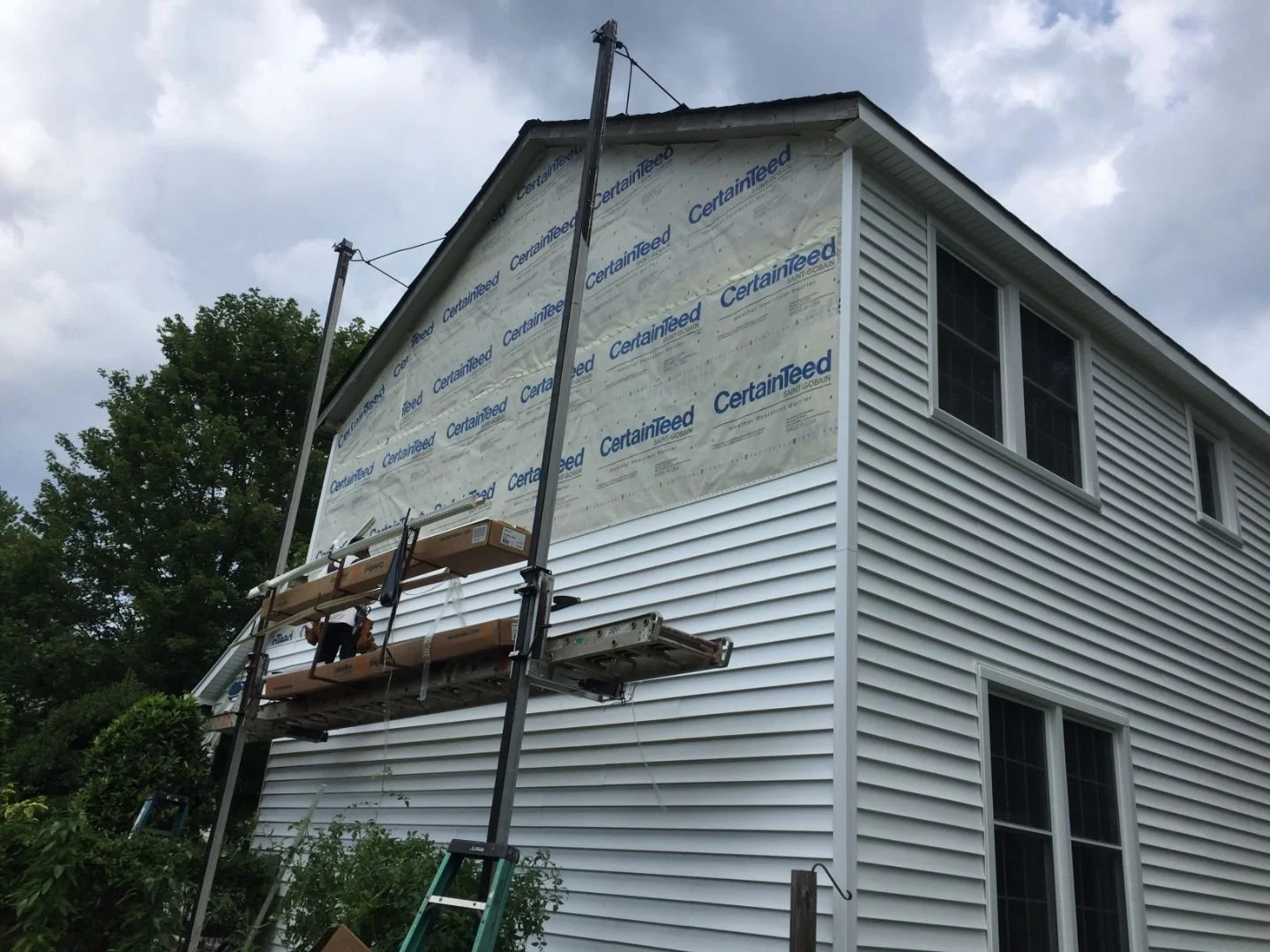 House undergoing exterior renovation with siding removal, scaffolding set up for workers, and a cloudy sky above.
