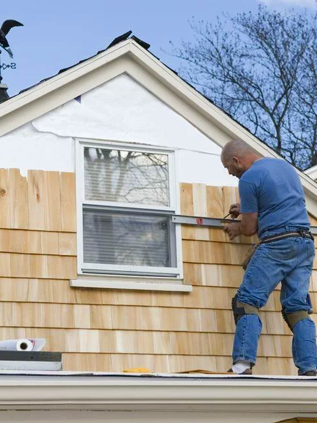 A man working on installing or repairing wooden siding on the exterior of a house, using a level tool.