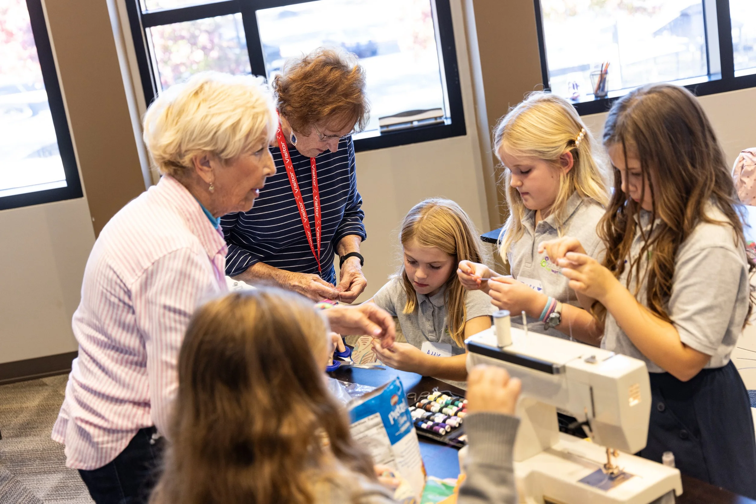 Group of children and adults working on a craft project in a classroom with large windows.
