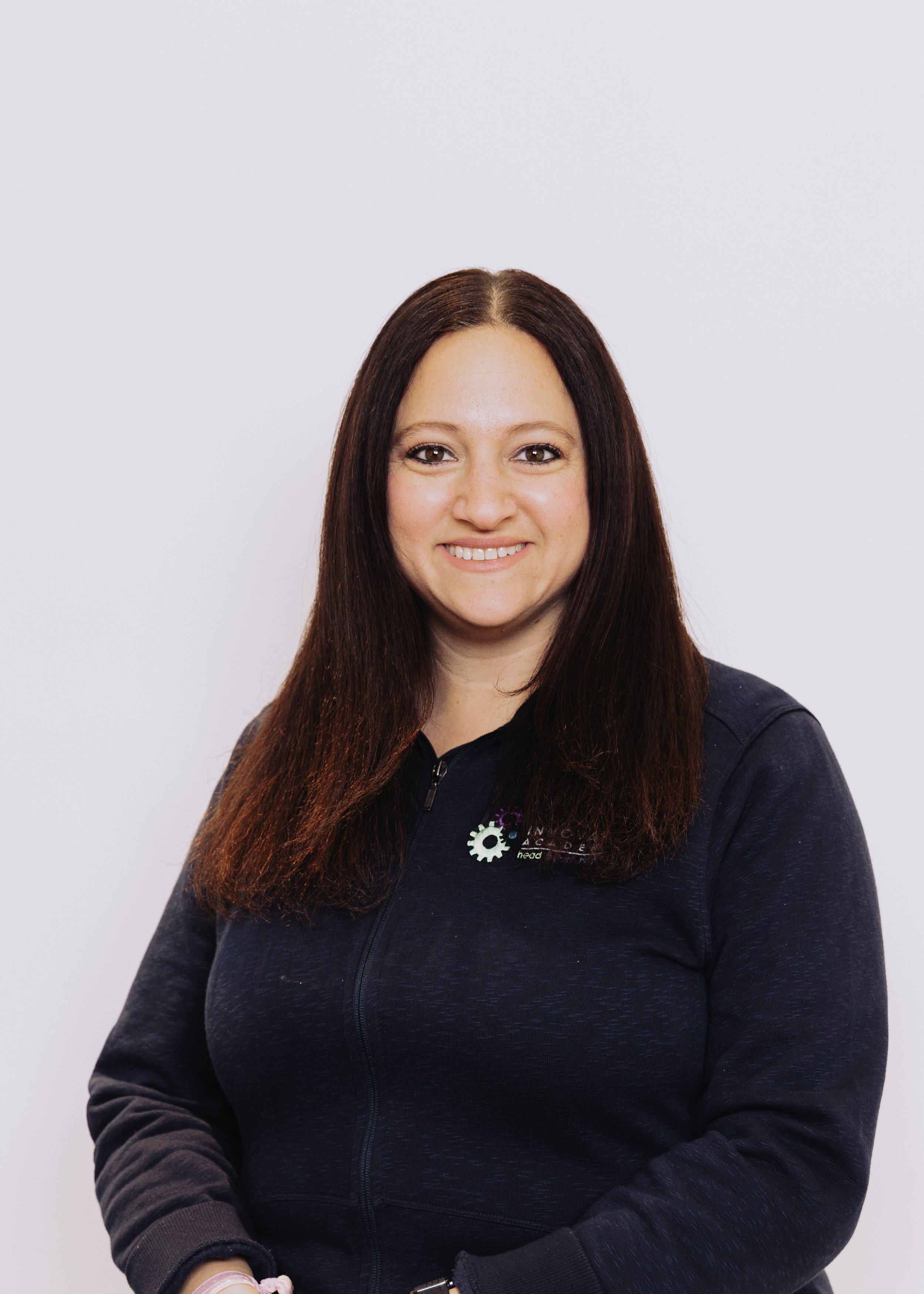 A woman with straight, long dark hair smiling at the camera, wearing a black zip-up jacket against a plain white background.