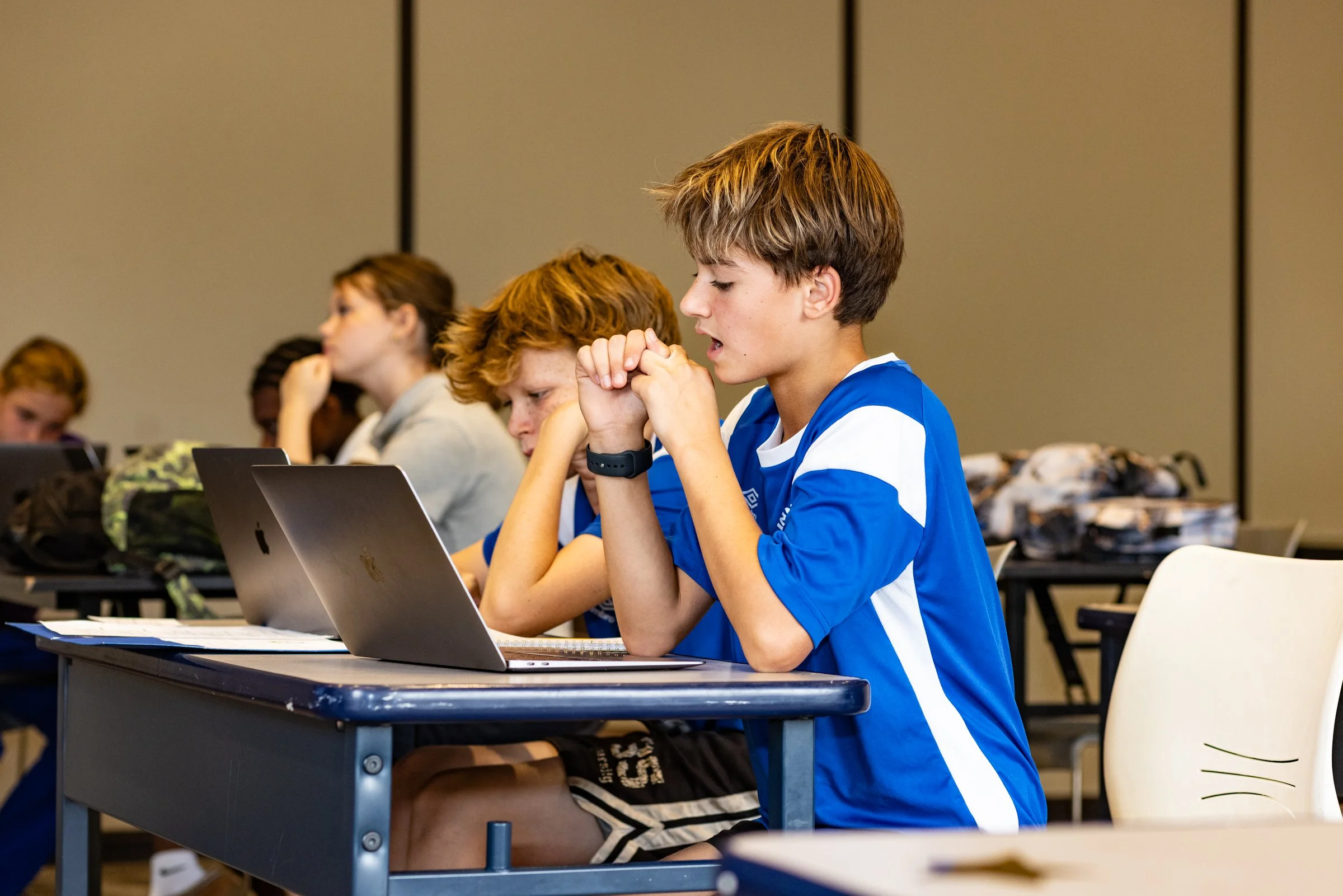 Students sitting at desks in a classroom, using laptops and appearing focused on their work.