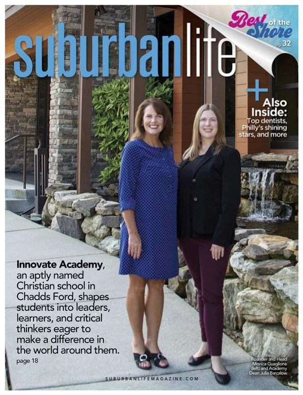 Cover of Suburban Life magazine featuring two women standing outdoors near a rock waterfall and greenery, with a building in the background. The woman on the left wears a blue dress, and the woman on the right wears a black blazer and maroon pants. The magazine highlights local topics including a Christian school in Chadds Ford and local stars.