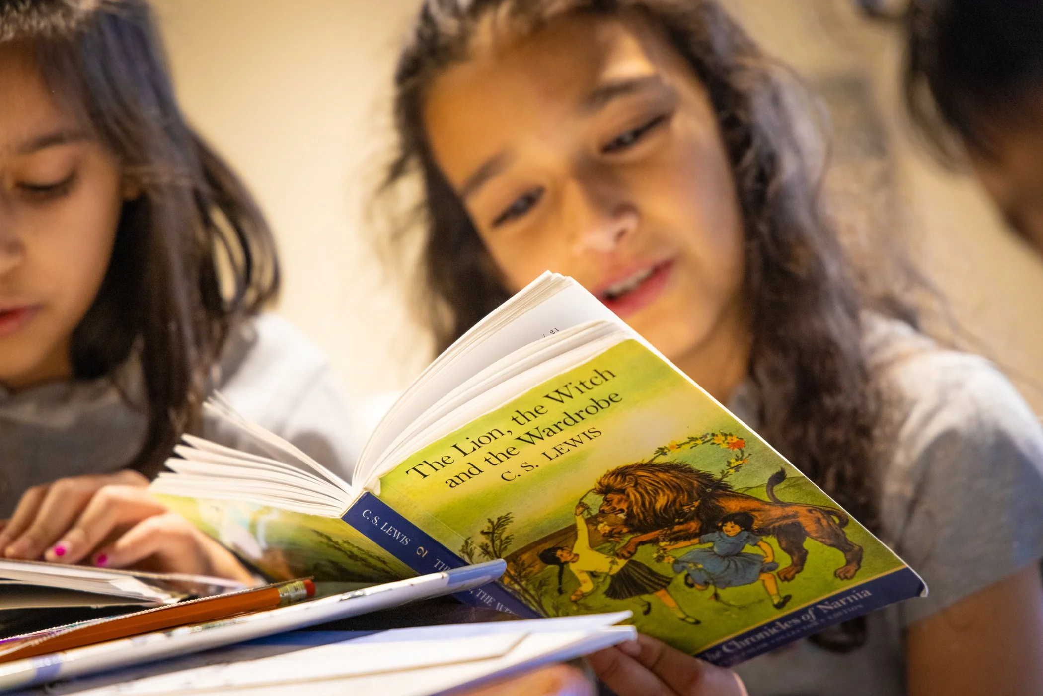 Three children reading a copy of "The Lion, the Witch, and the Wardrobe" by C.S. Lewis.