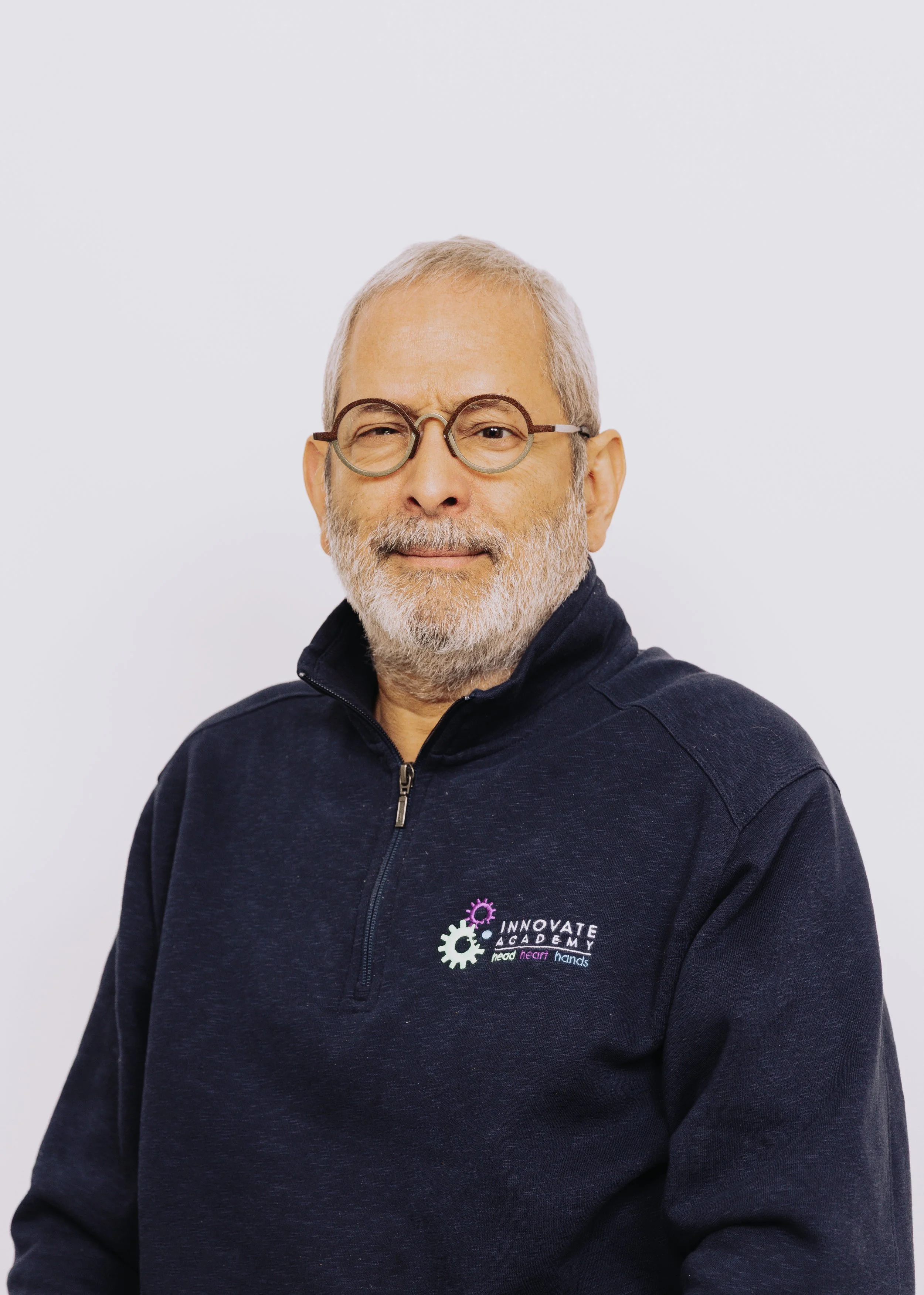 A middle-aged man with glasses and gray hair, wearing a navy blue quarter-zip sweatshirt with an "Innovate Academy" logo, standing against a white background.