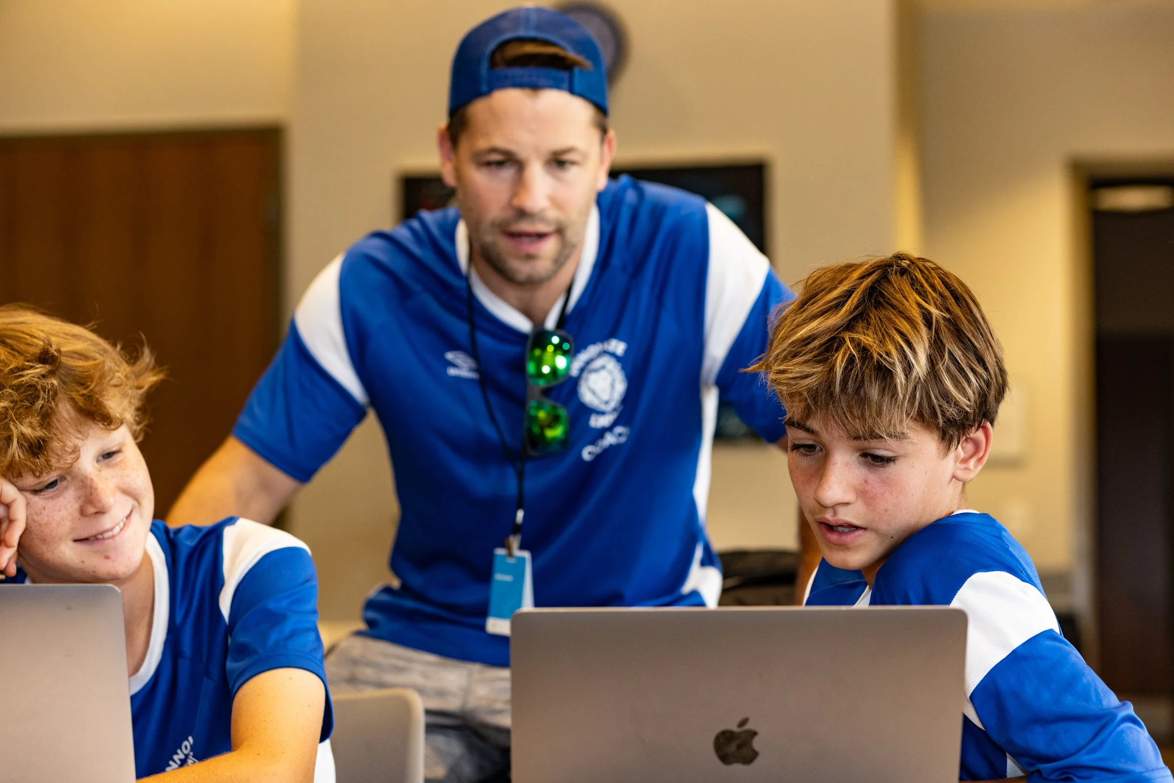 A man with two young boys working on laptops in a classroom or computer lab.