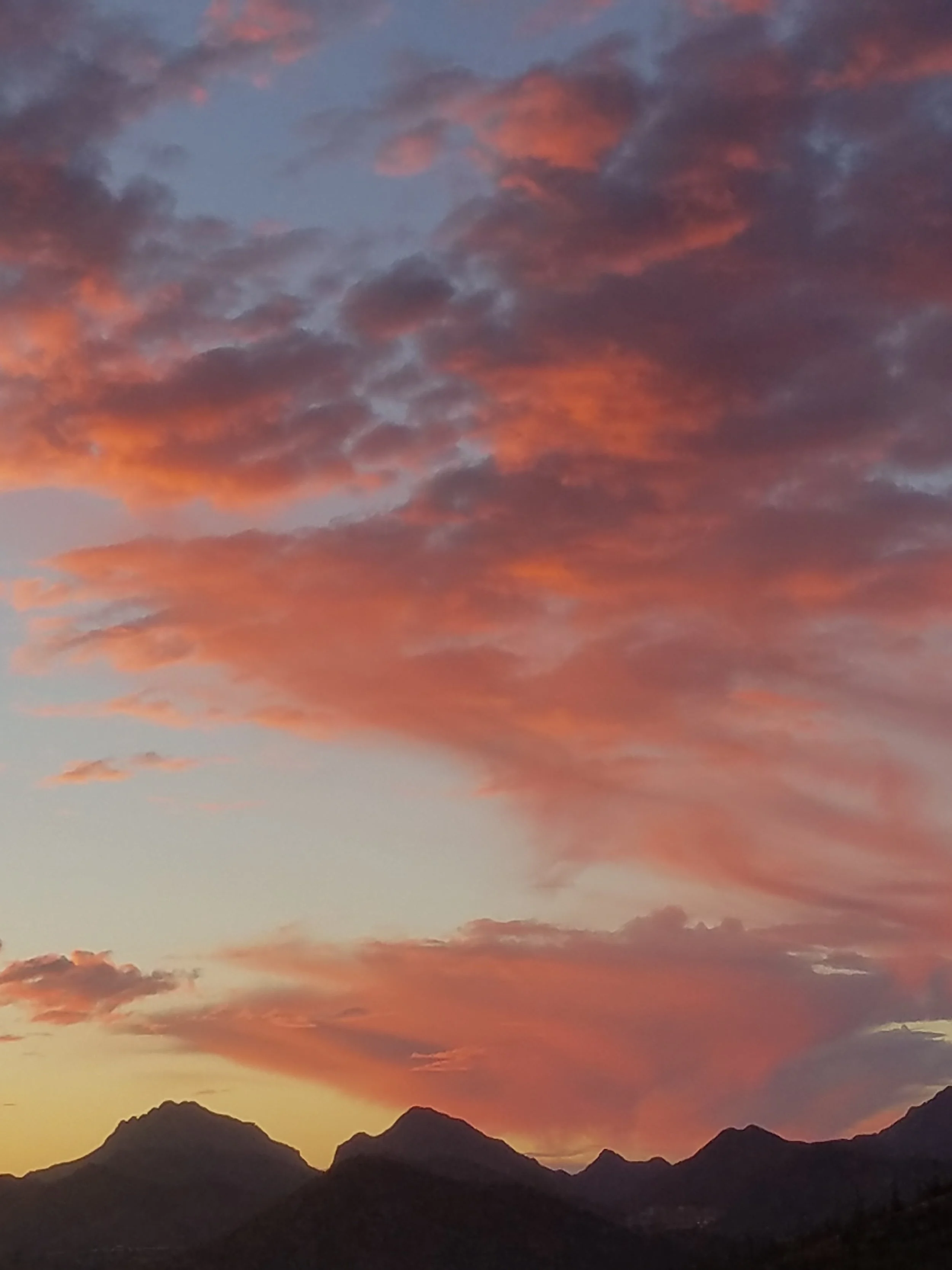 Sunset over mountain silhouettes with colorful orange, pink, and purple clouds in the sky.