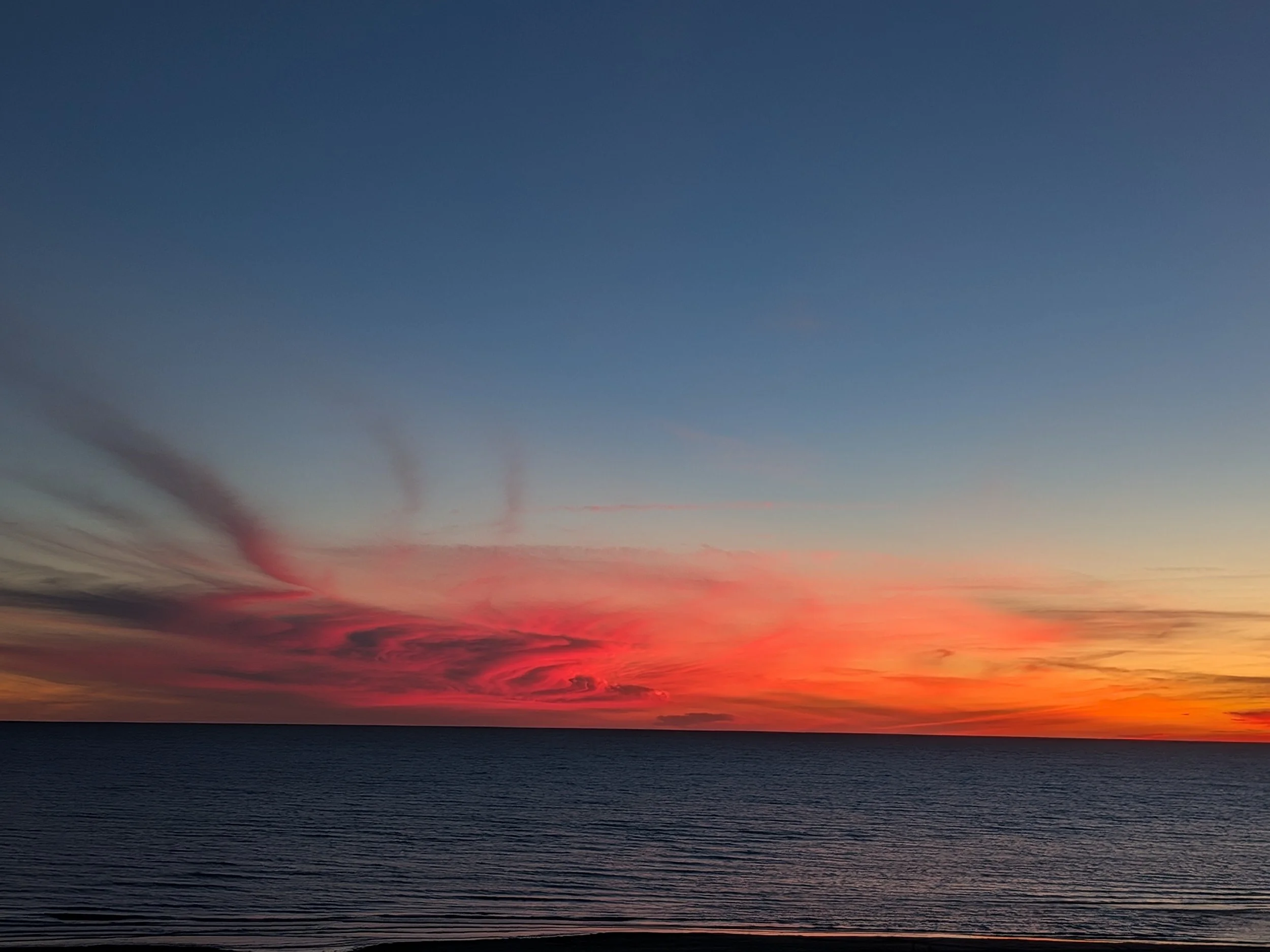 A sunset over calm ocean water with colorful pink, orange, and blue sky and streaks of clouds.