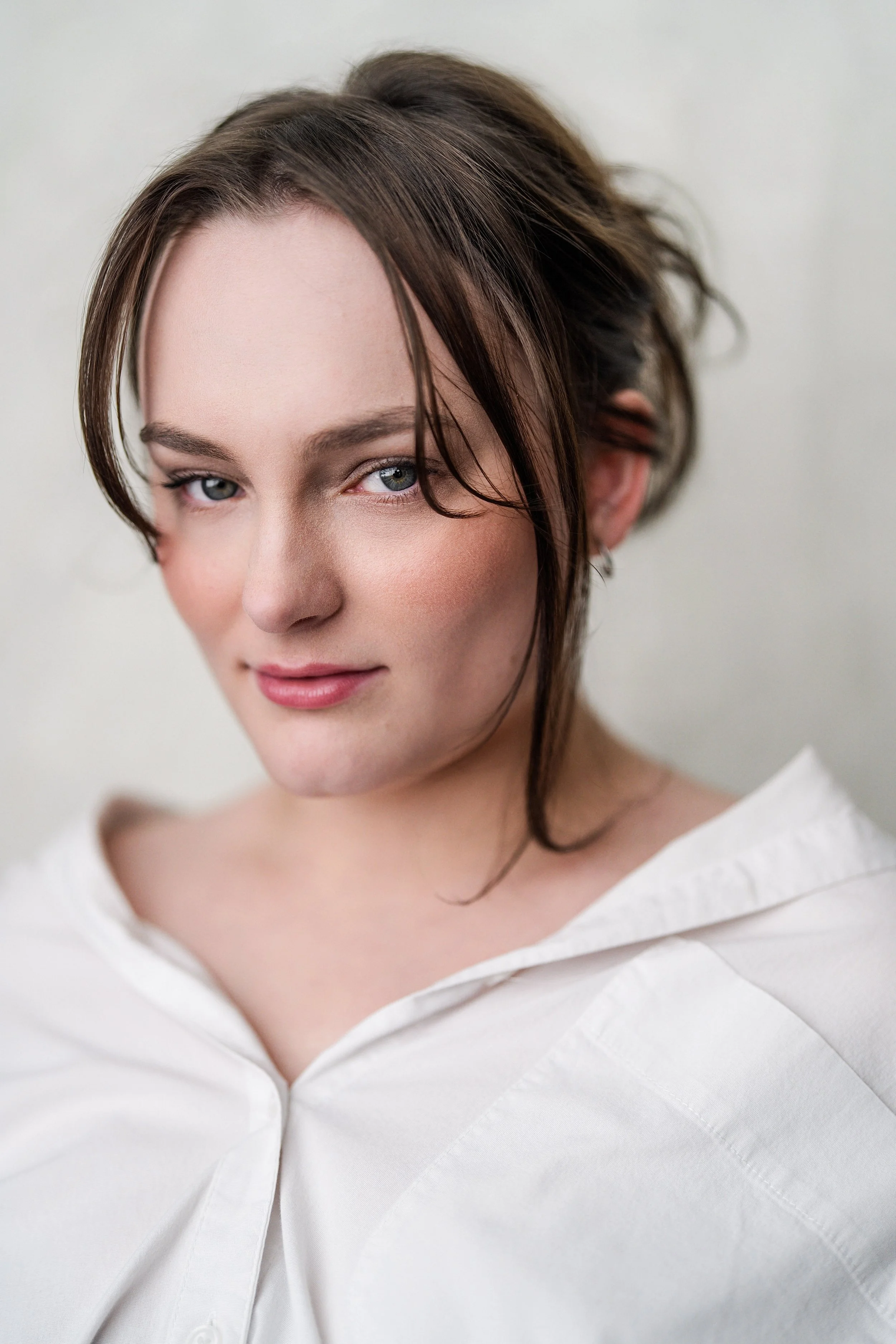 Close-up portrait of a young woman with brown hair, wearing a white shirt, looking at the camera with a slight smile.
