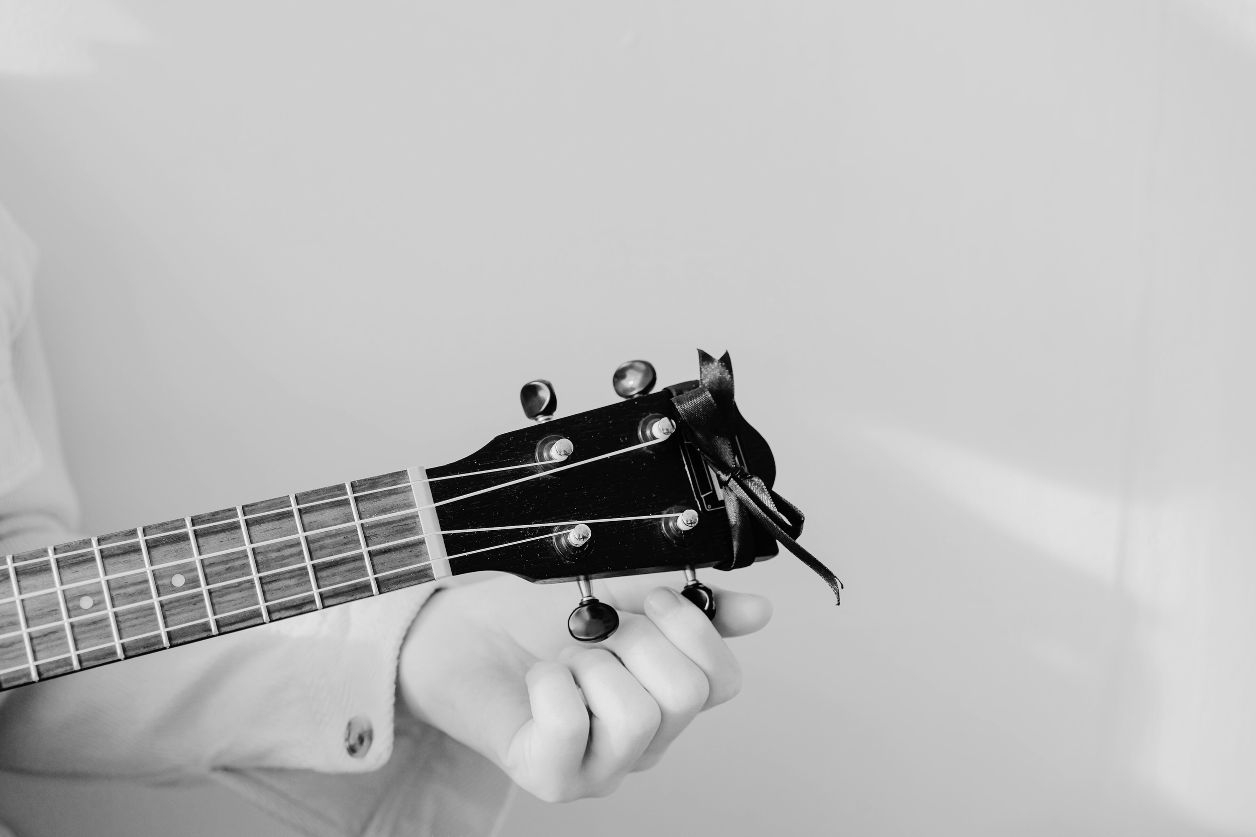A person holding the headstock of a guitar with a ribbon tied around it in black and white.