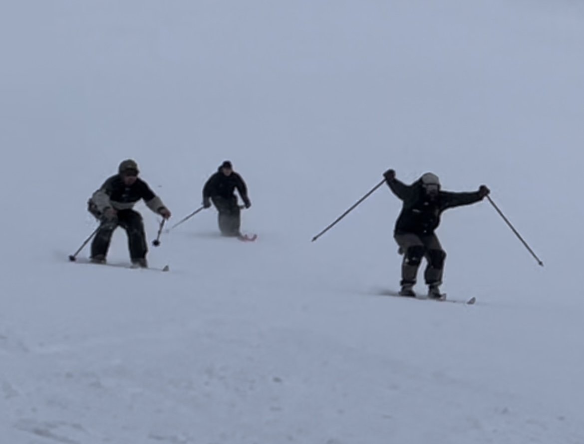 Three people in winter gear skiing on a snowy slope.