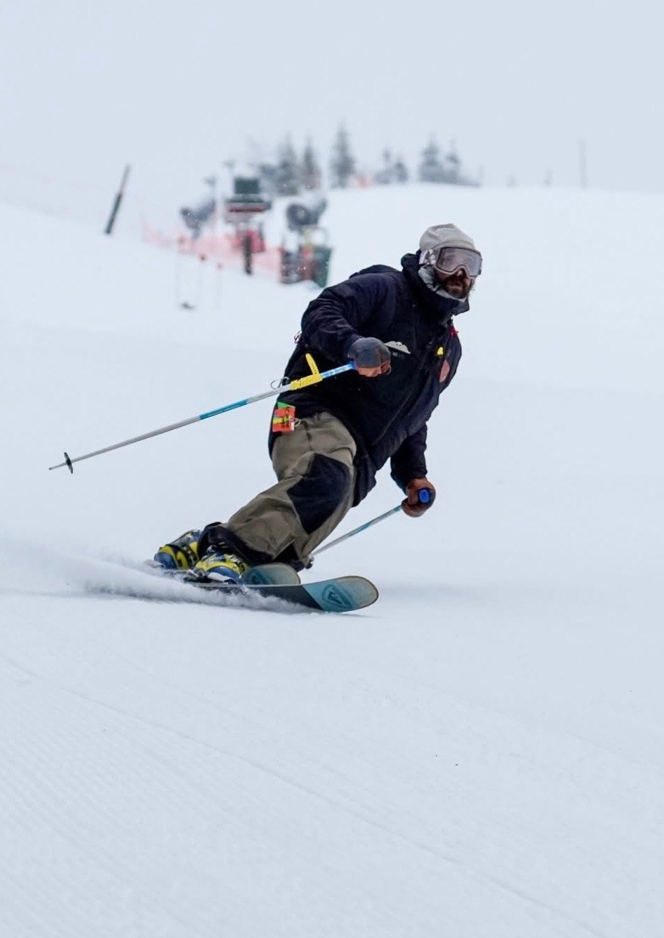 Person skiing in snowy conditions wearing goggles, a helmet, and winter gear, with a ski lift in the background.