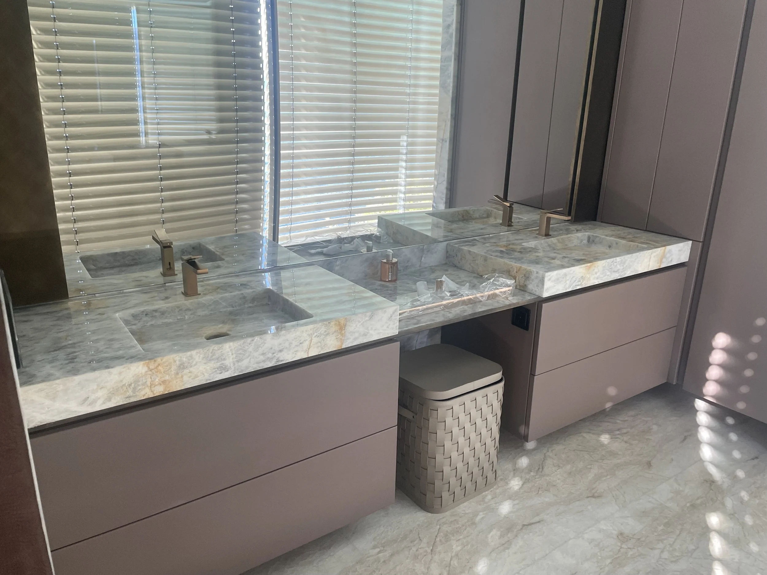 Due lavandini in pietra con rubinetti moderni, specchi e armadietti in una stanza da bagno luminosa con luci naturali