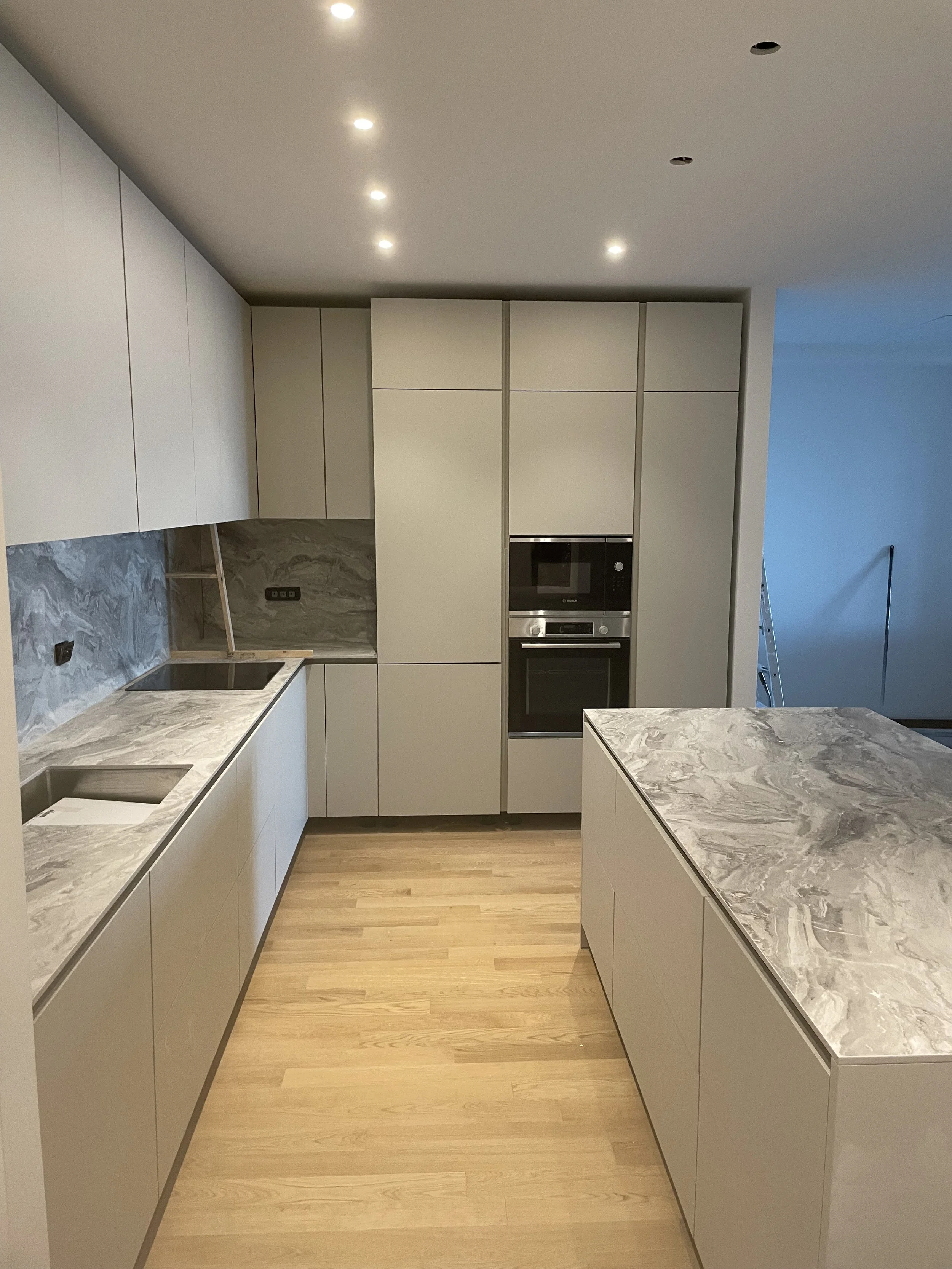 Cucina moderna con pensili bianchi, piano in marmo grigio, elettrodomestici incorporati e pavimento in legno.