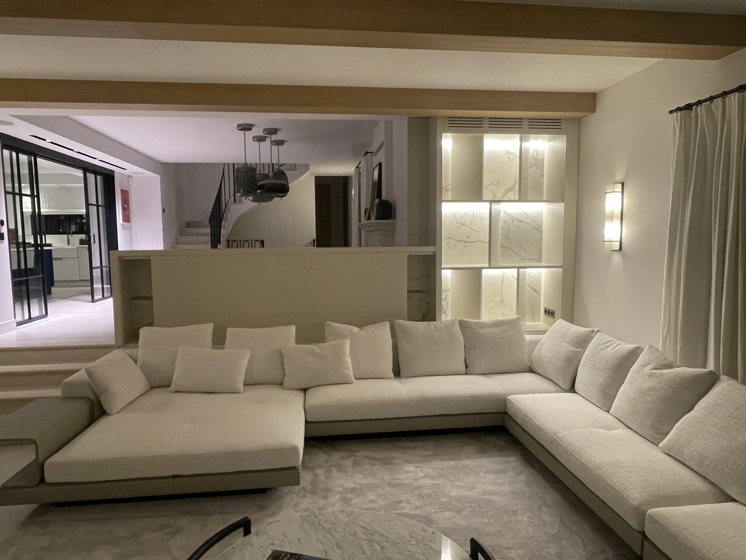 Soggiorno con divano bianco ad angolo, tappeto grigio chiaro, pareti bianche, con parete decorativa illuminata in background e divano bianco.