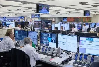 Stock trading floor with multiple traders working at computers with financial charts and screens.