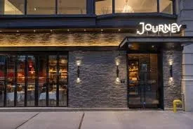 Exterior view of a restaurant named 'Journey' with black brick facade, glass doors, and warm lighting inside.