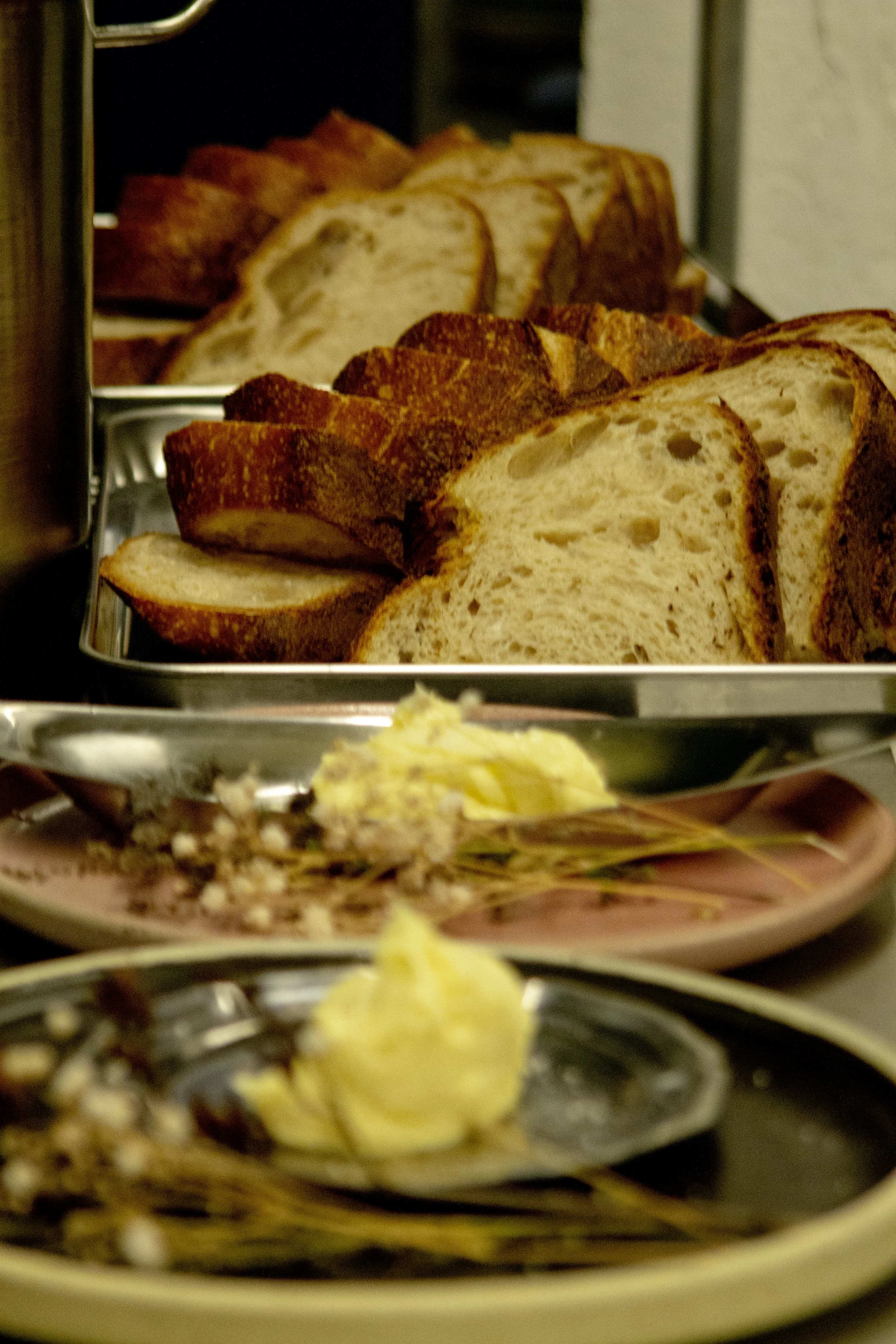 Slices of bread on a metal tray with butter and a platter of scrambled eggs on the side.