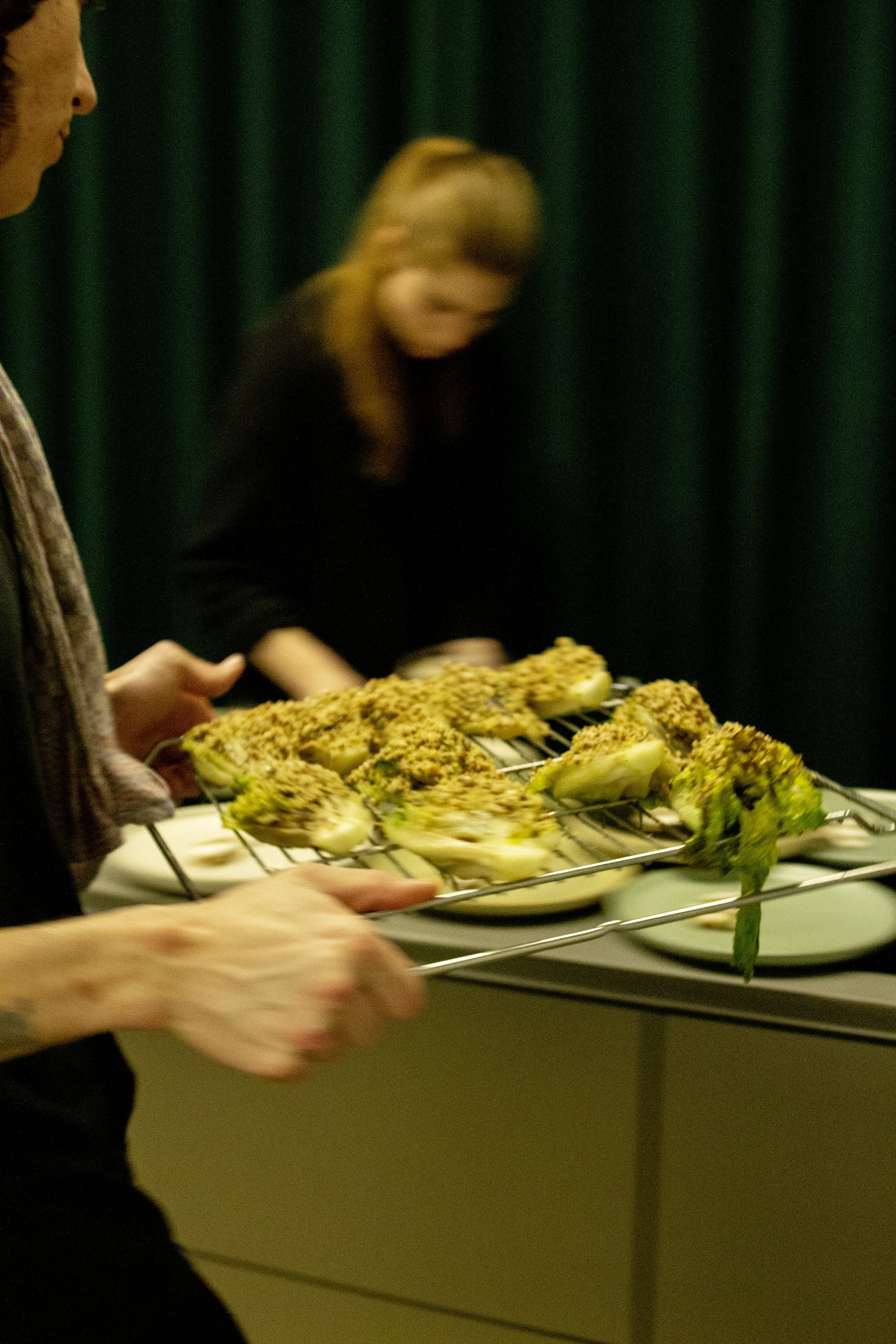 People placing baked stuffed artichokes on a platter at a buffet.