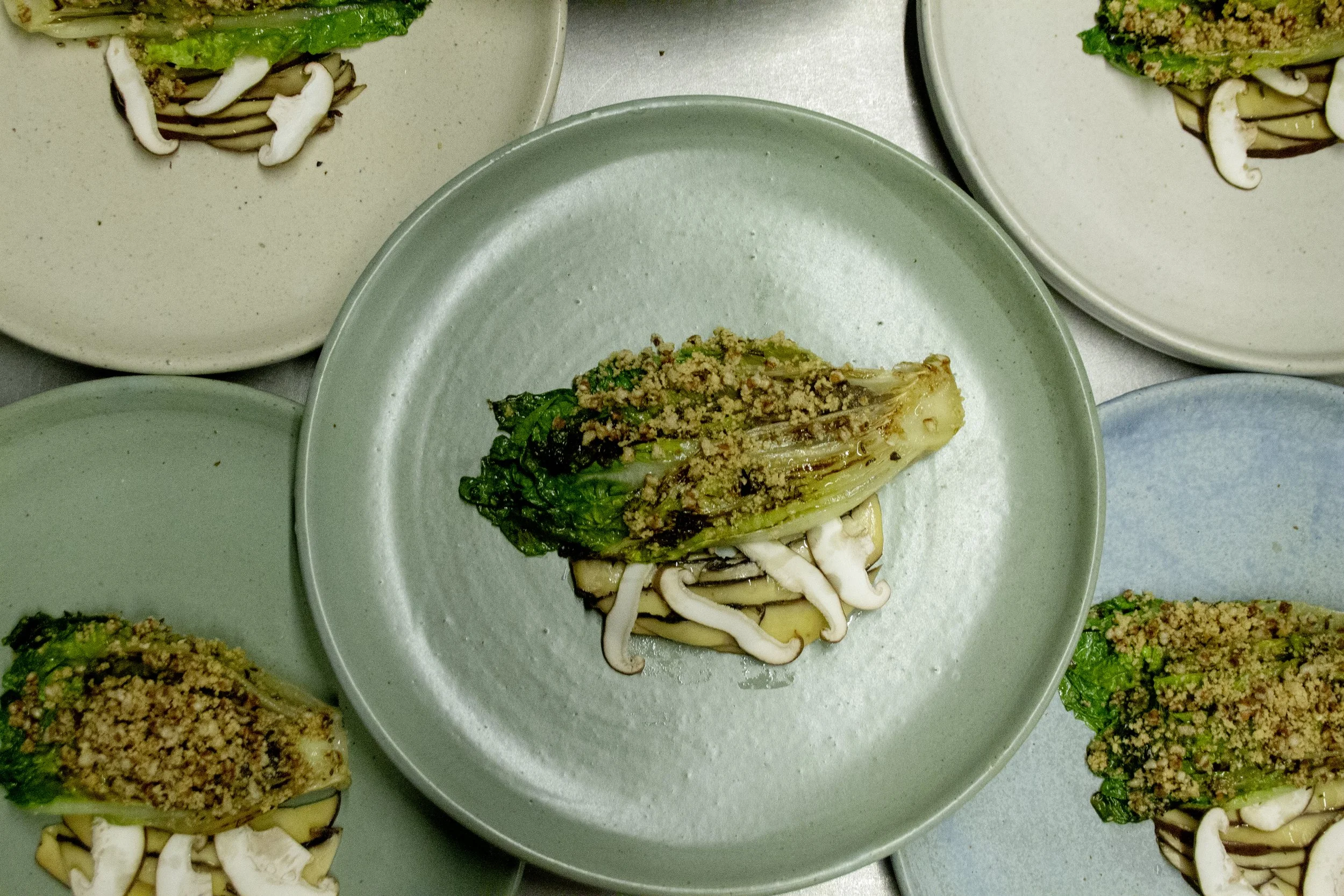 Plated dish featuring grilled romaine lettuce topped with ground meat, served over sliced zucchini and enoki mushrooms.