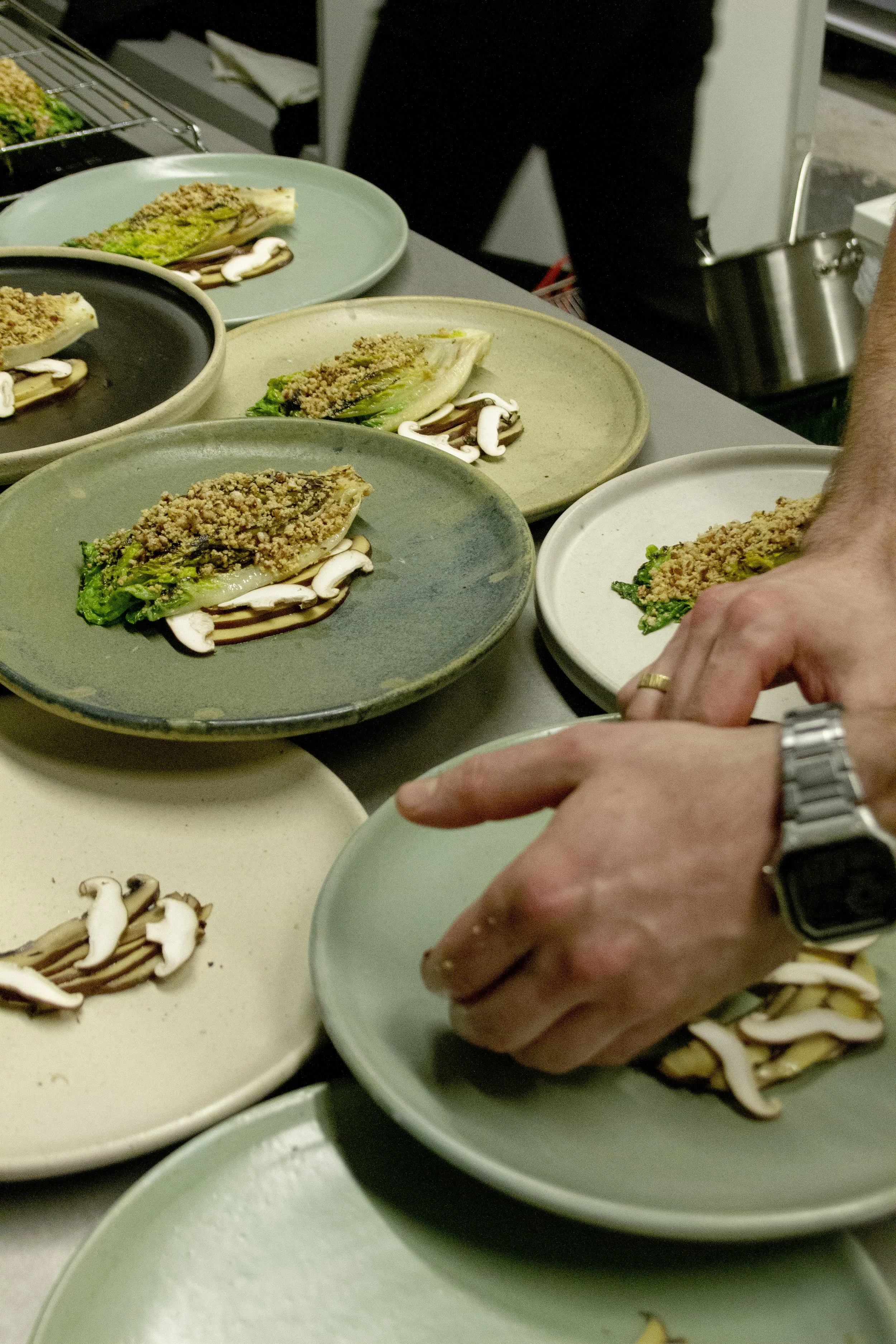 Plates of lettuce wraps topped with crushed peanuts, sliced mushrooms, and drizzled with sauce, being prepared at a kitchen counter.