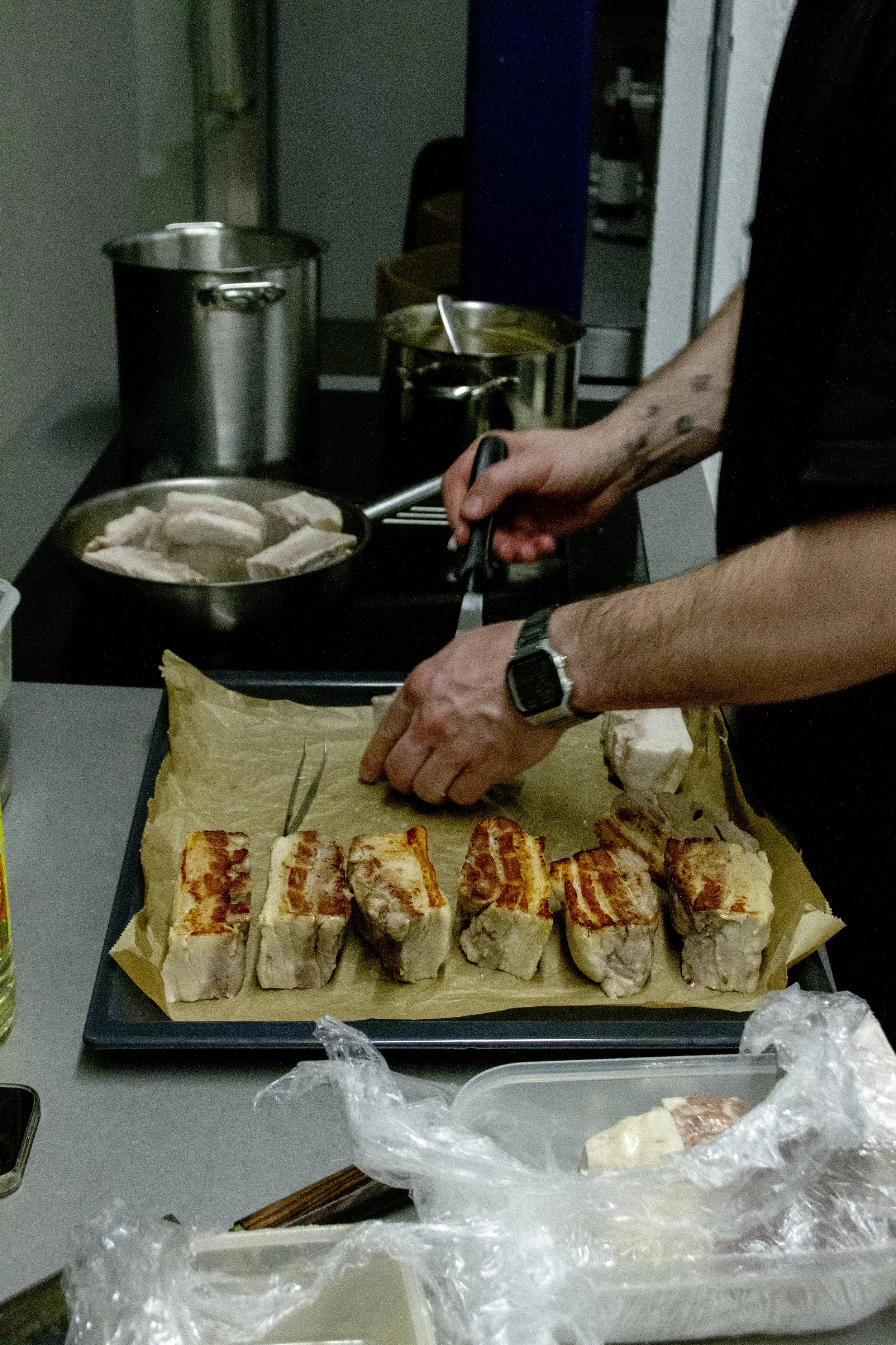 Person preparing grilled pork belly slices on a tray in a kitchen.