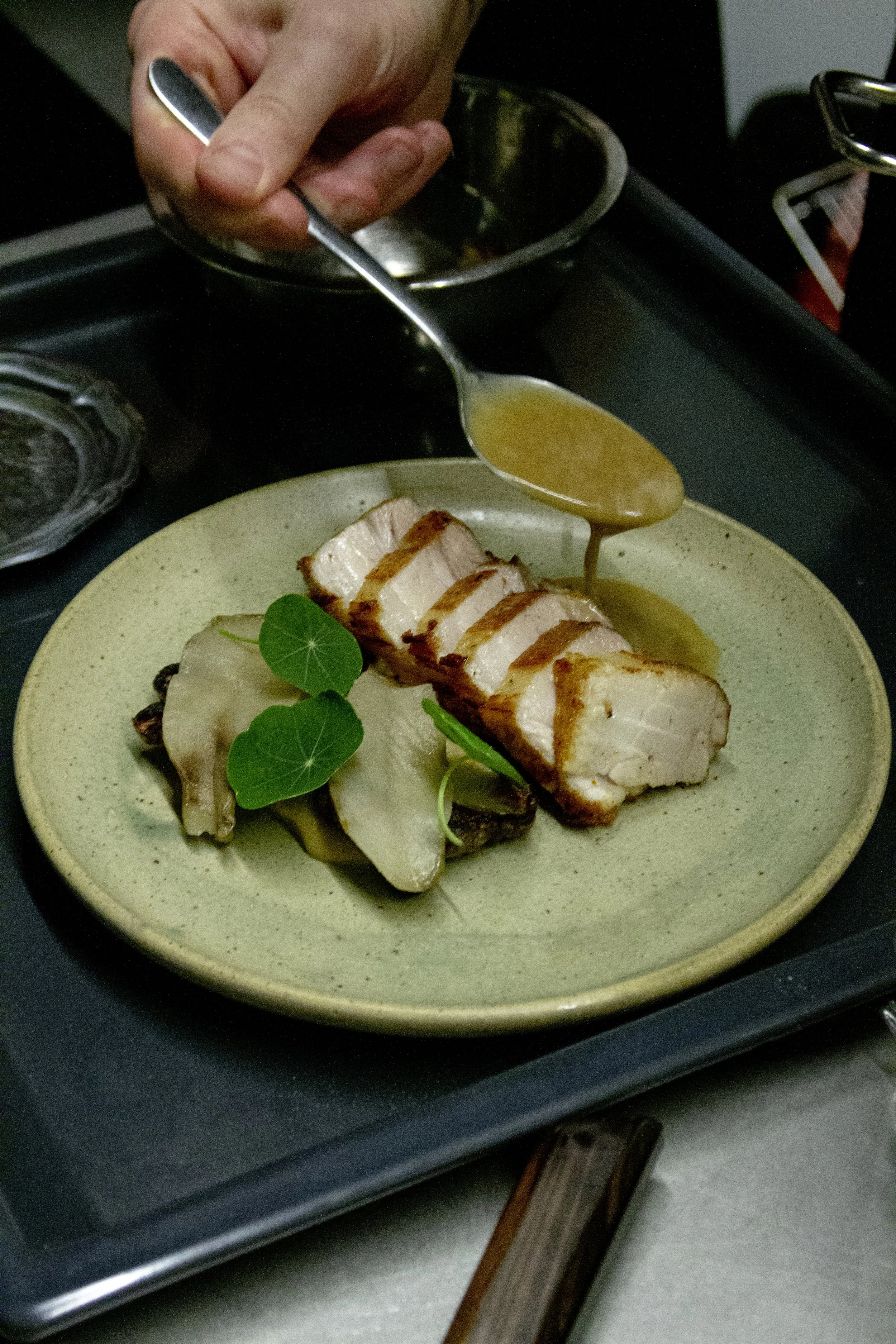Close-up of a plated dish with sliced chicken breast topped with sauce, garnished with green leaves, and served with potato slices on a beige plate.
