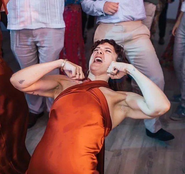 Woman in a burnt orange satin dress fighting or posing aggressively at a party or social gathering.