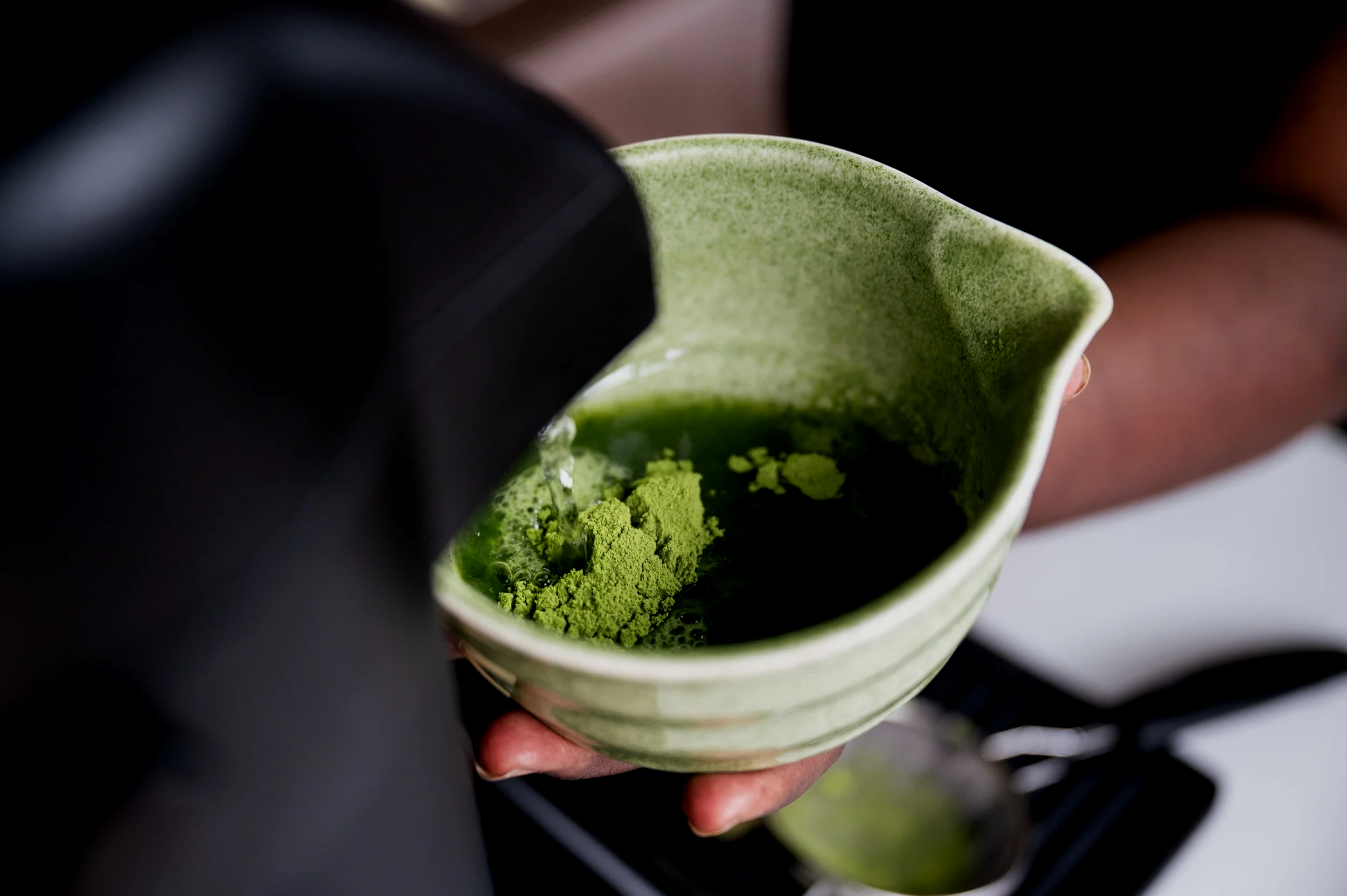 Person holding green ceramic bowl with matcha tea powder and liquid inside