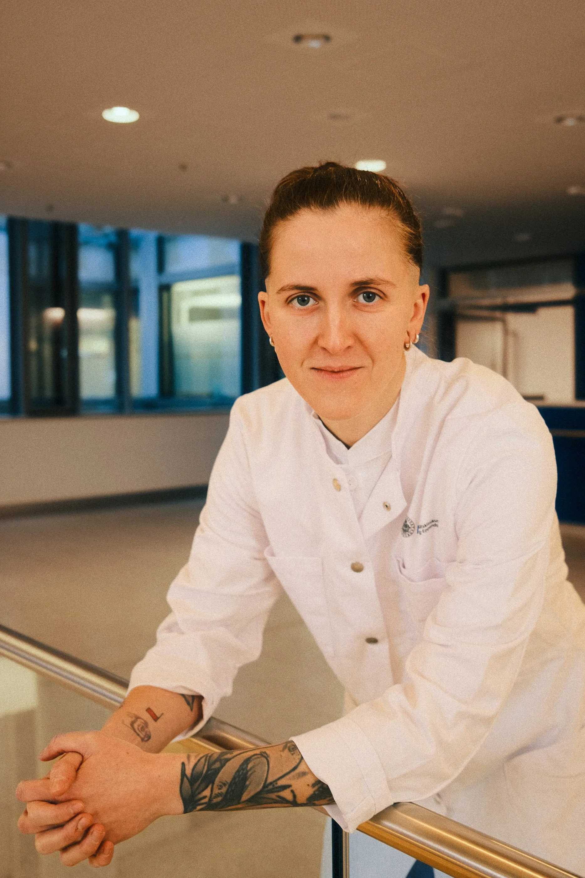 A person in a white uniform leaning on a hospital counter, indoors with windows in the background.