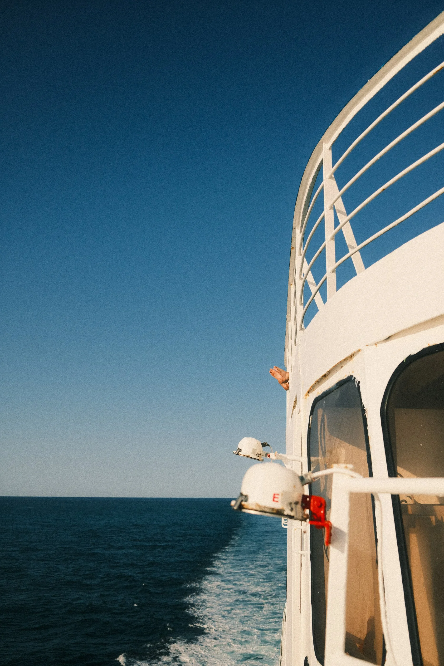 View of a boat's deck with a white railing, two white navigational lights, and a clear blue sky over the ocean.