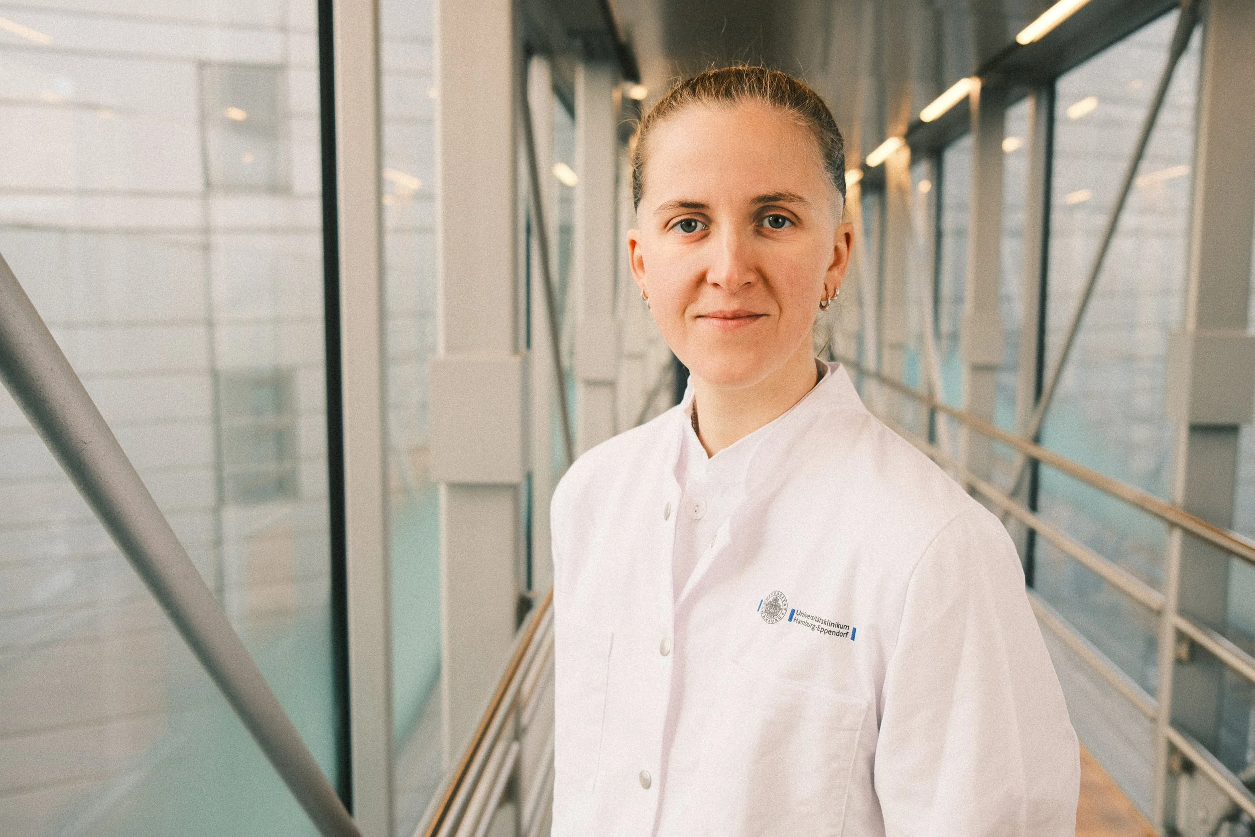 A person in a white medical coat standing in a modern hospital corridor.