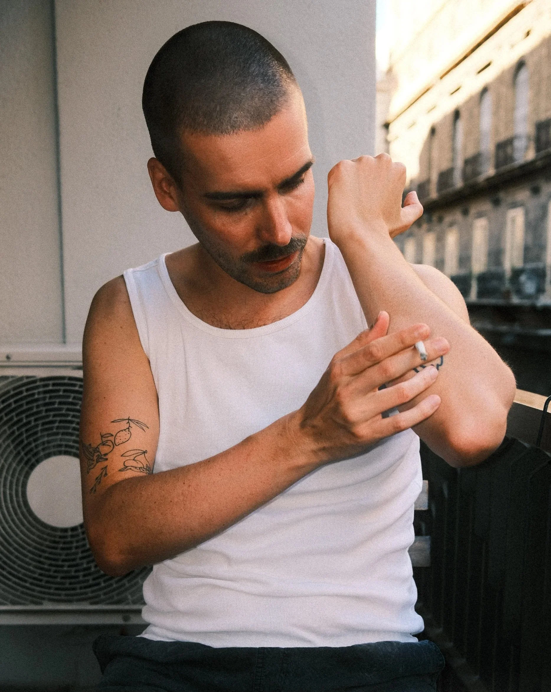 Mann auf Balkon sitzen mit Zigarette und Tattoo in Unterhemd