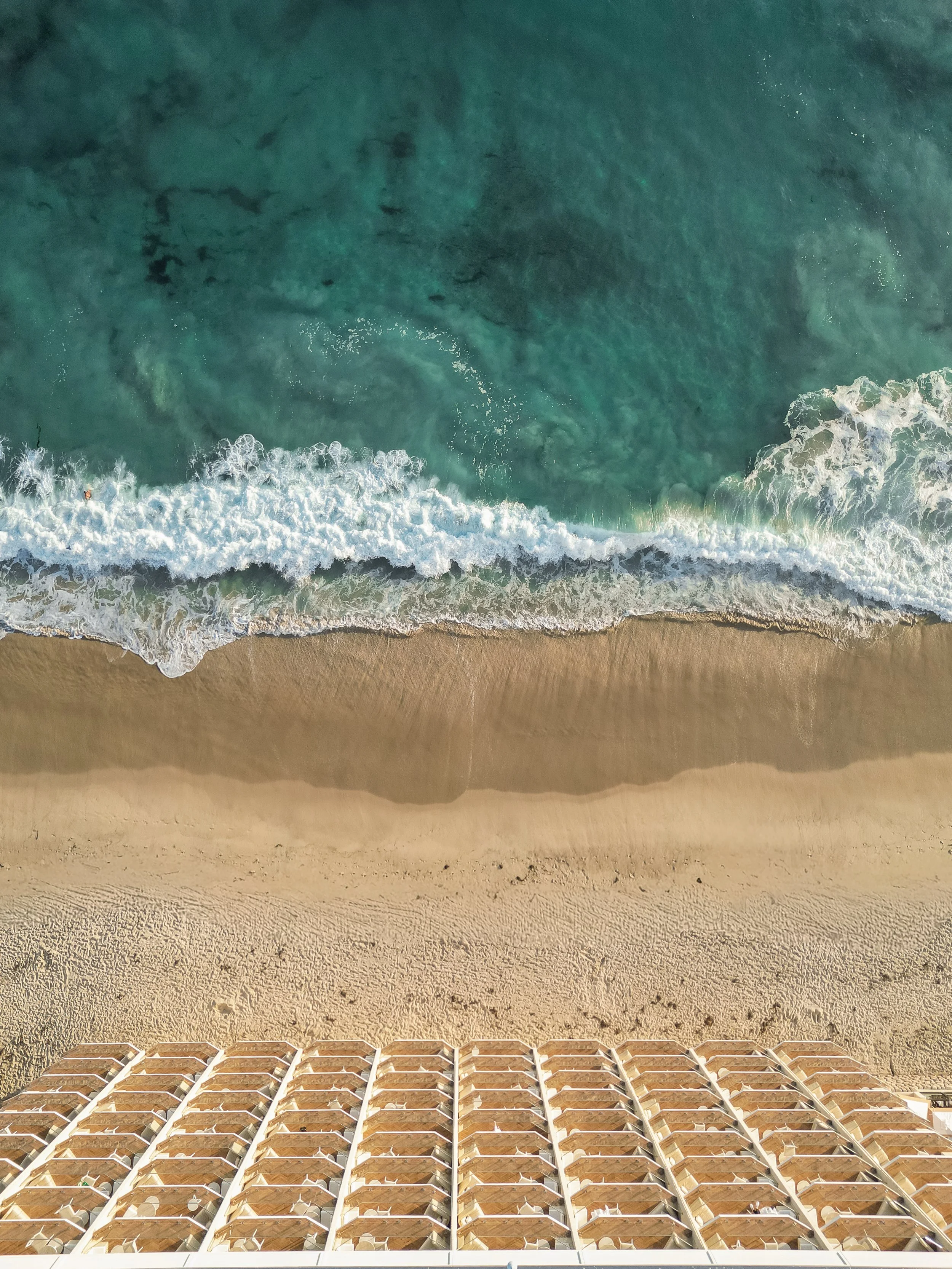 Aerial view of a beach with lounge chairs, sandy shore, and waves crashing in the ocean.