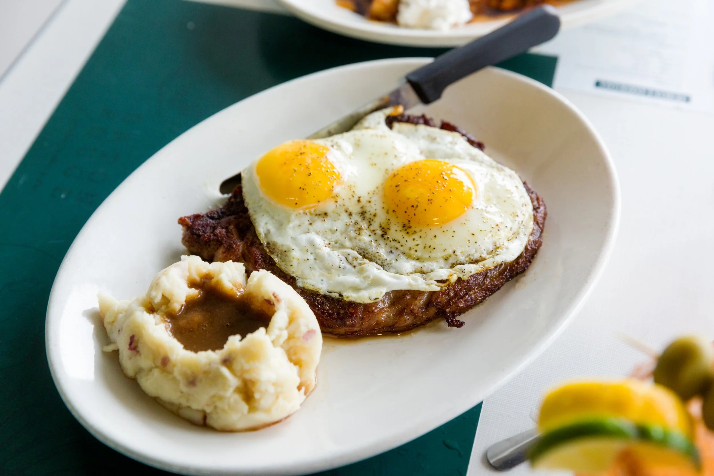 A plate of breakfast with two fried eggs, sunny-side up, on a piece of steak, served with mashed potatoes and gravy.