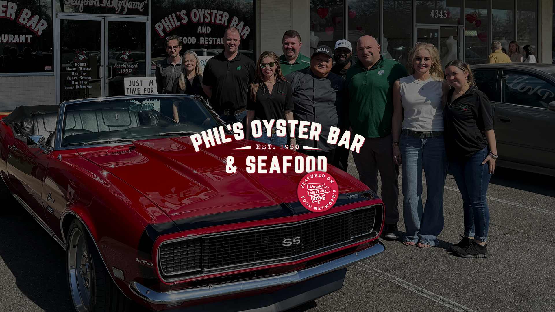 A group of smiling employees at Phil's Oyster Bar and Seafood are posing behind a vintage red convertible. Overlaid text reads 'Phil's Oyster Bar & Seafood, Est. 1950.' with Food Network's Diners, Drive-Ins, Drives logo.