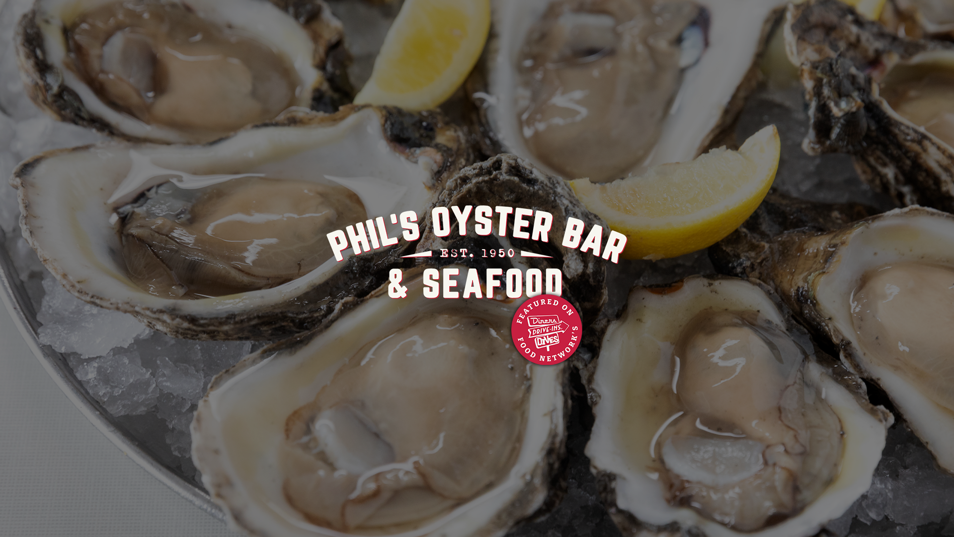 Close-up of fresh oysters on ice with lemon wedges at Phil's Oyster Bar & Seafood. Overlaid text reads 'Phil's Oyster Bar & Seafood, Est. 1950.' with Food Network's Diners, Drive-Ins, Drives logo.