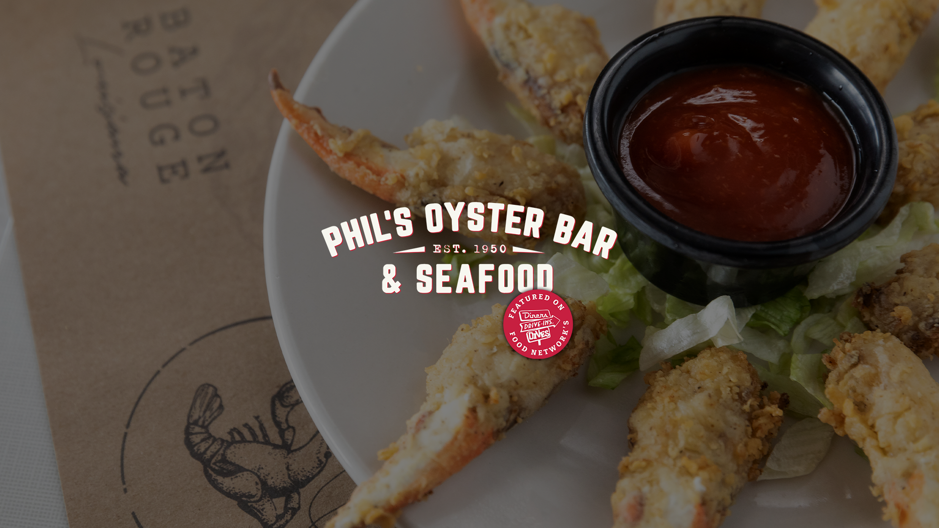 Fried crab claws with a container of dipping sauce on a white plate. Overlaid text reads 'Phil's Oyster Bar & Seafood, Est. 1950.' with Food Network's Diners, Drive-Ins, Drives logo.