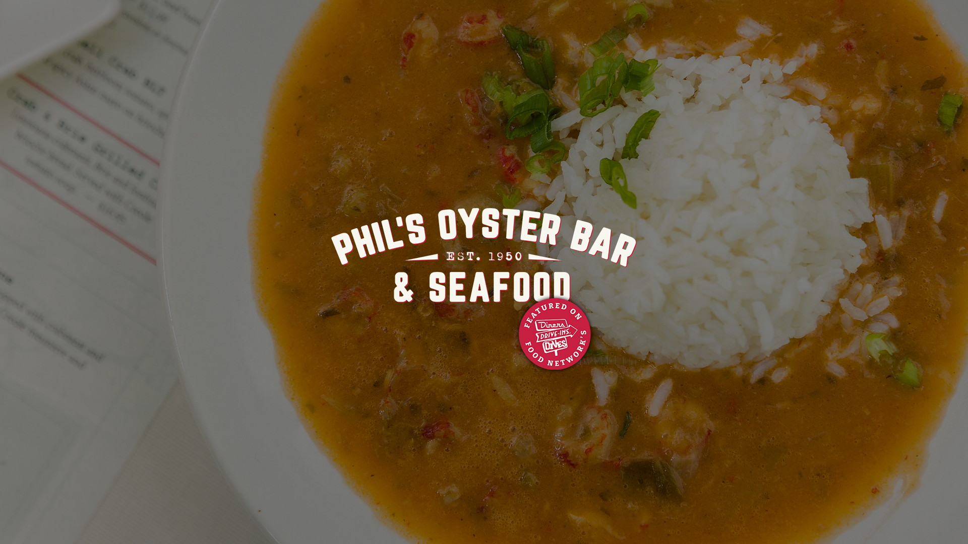 A bowl of seafood gumbo with rice, garnished with chopped green onions. Overlaid text reads 'Phil's Oyster Bar & Seafood, Est. 1950.' with Food Network's Diners, Drive-Ins, Drives logo.