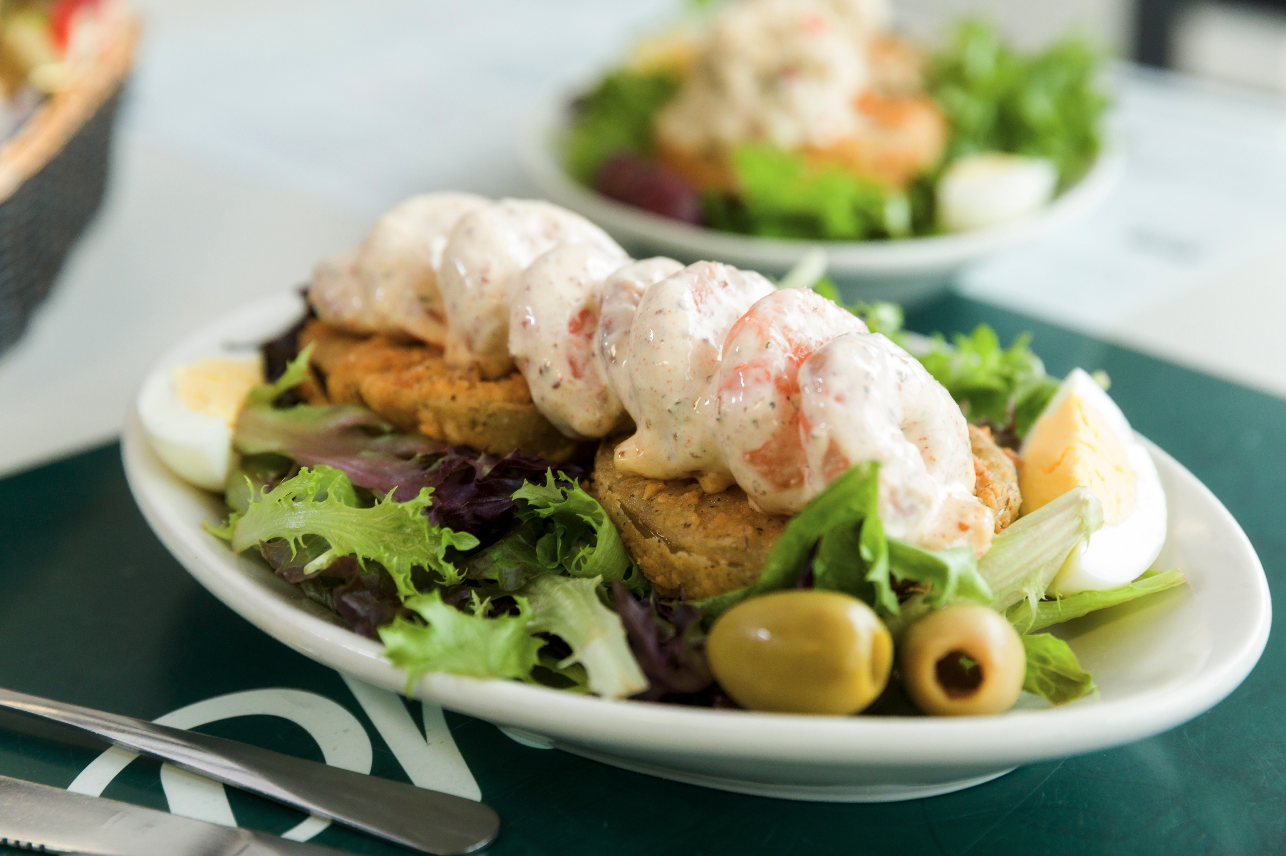 Salad with sliced fried green tomatoes, boiled eggs, green olives, lettuce, and a creamy topping, served on a white plate.