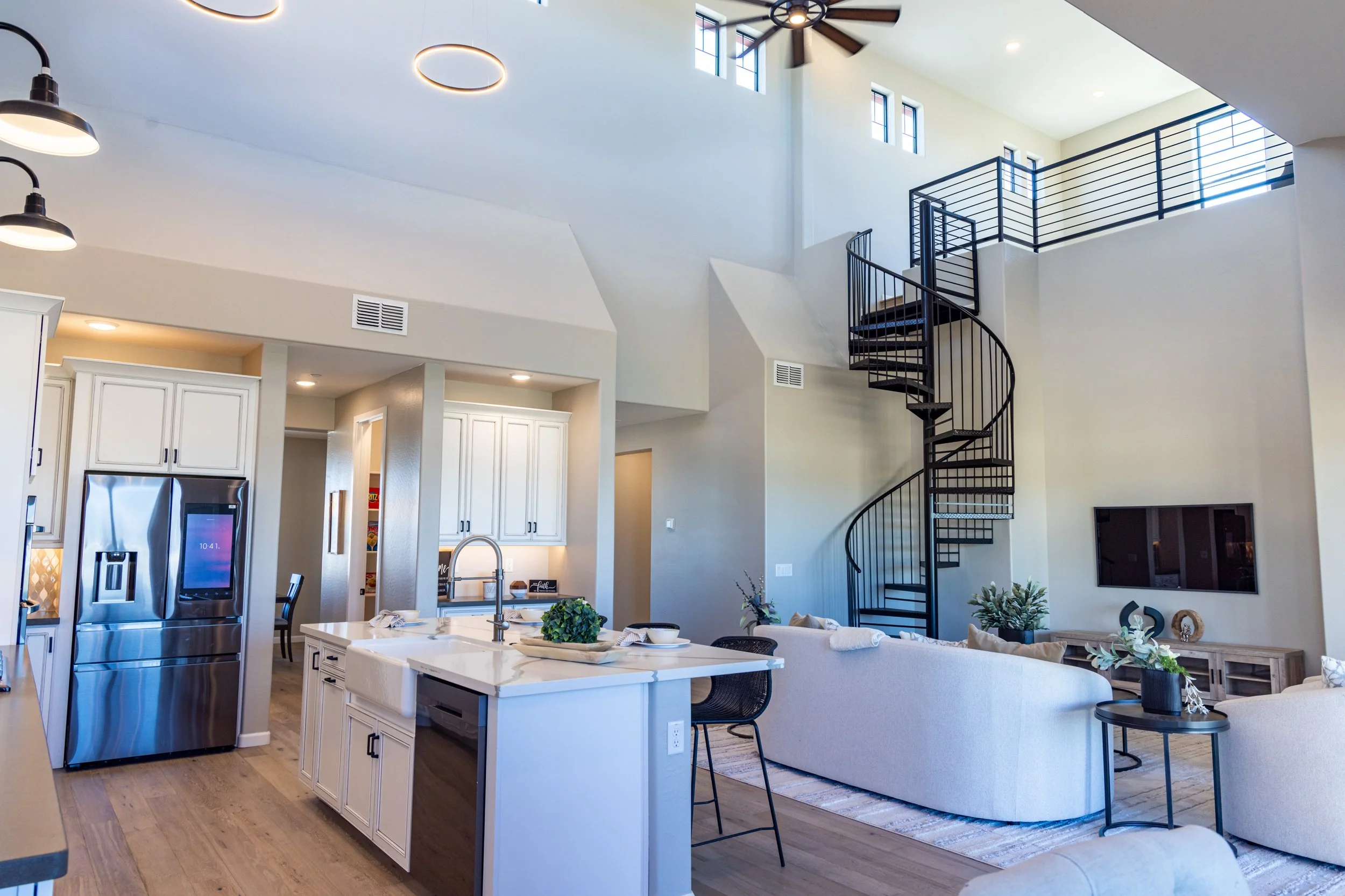 Open-concept living room and kitchen with high ceilings, modern furnishings, and a spiral staircase.