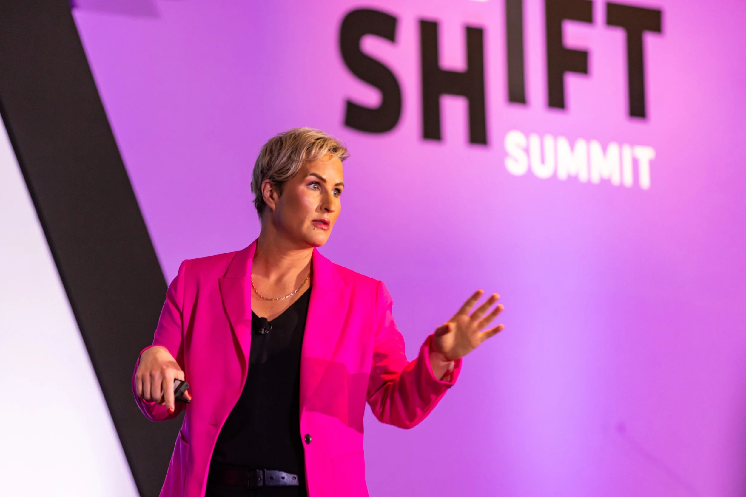 A woman with short blonde hair and a pink blazer giving a presentation at the Shift Summit event.