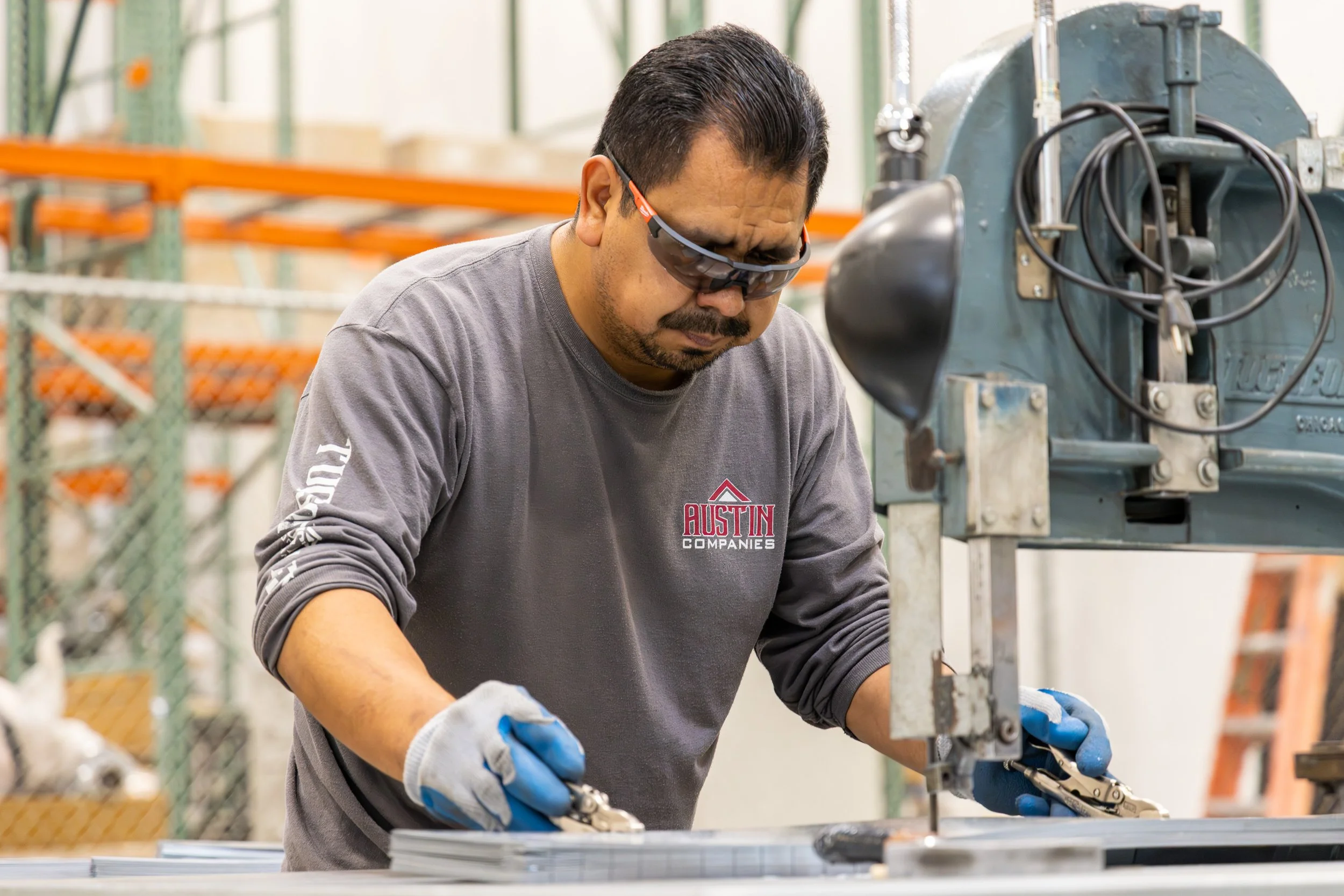 A worker wearing safety glasses and gloves uses a machine to cut or shape metal sheets in a factory or workshop.