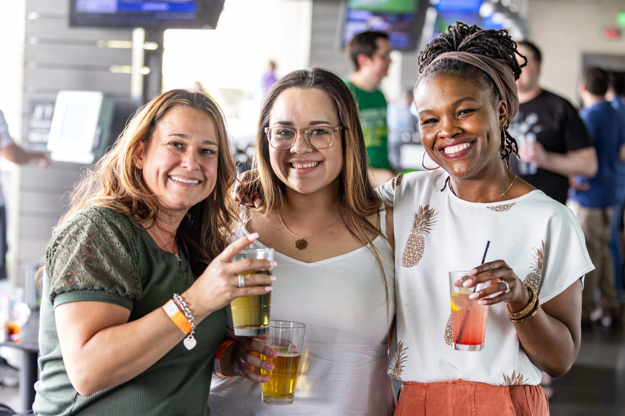 Three women smiling and holding drinks at a social gathering or party.