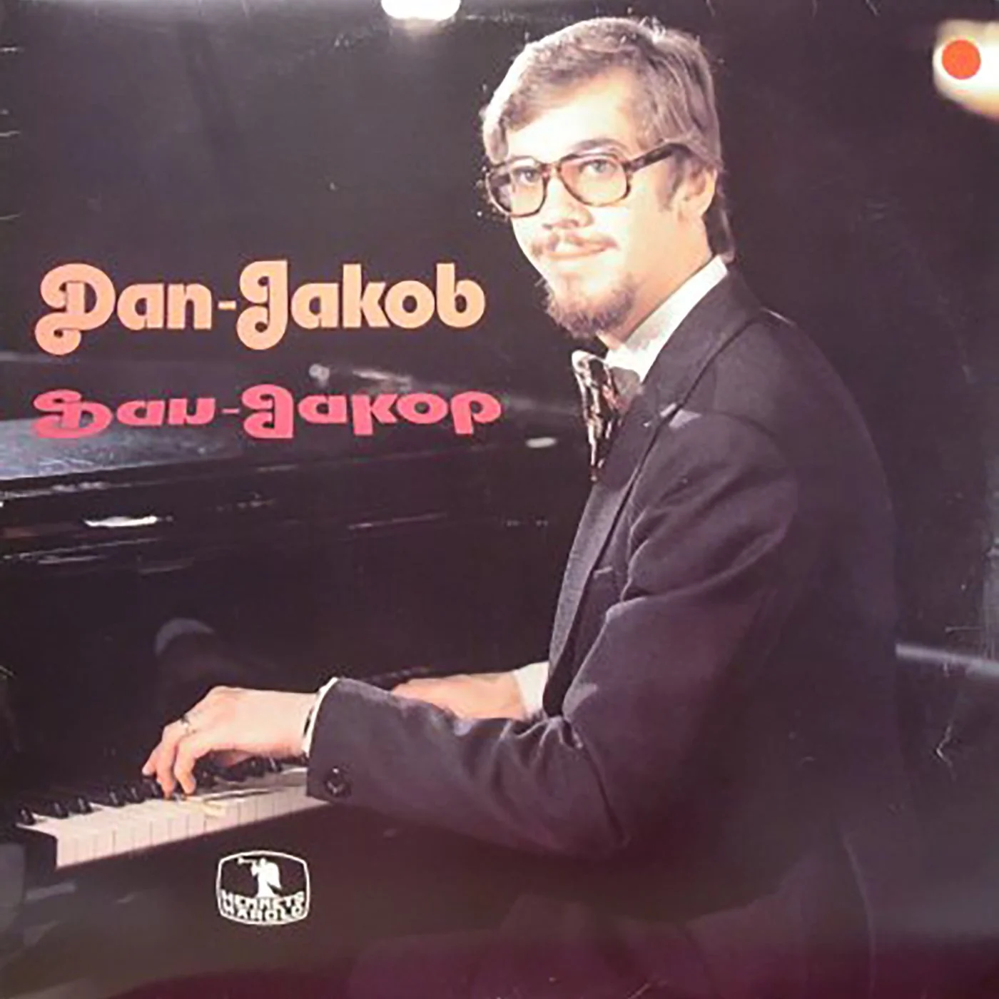 En man i glasögon och svart kostym som spelar piano.