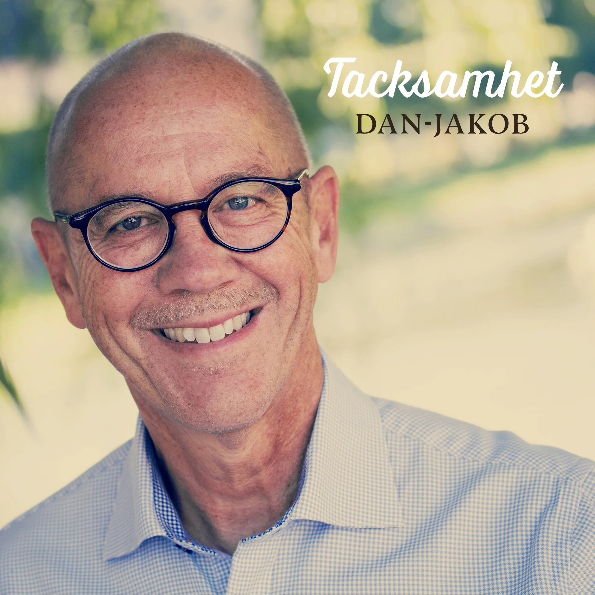 En man med glasögon och blå skjorta, ler mot kameran. Texten på bilden är 'Tacksamhet DAN-JAKOB'.