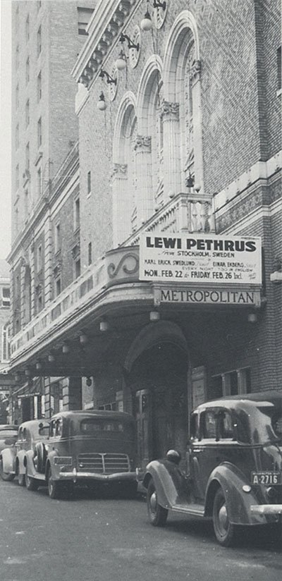 Svartvitt foto av ett teaterskylt för Lewi Pethrus med ett evenemang i Stockholm, Sverige, samt oldbilar parkerade längs gatan i förgrund.