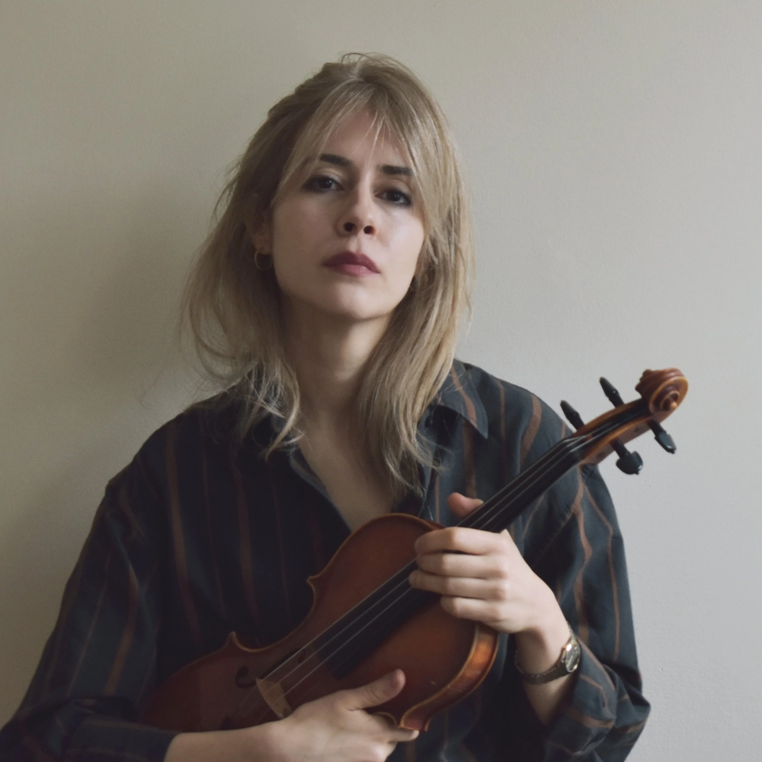 A blonde woman posing with her violin against a blank backgroud.